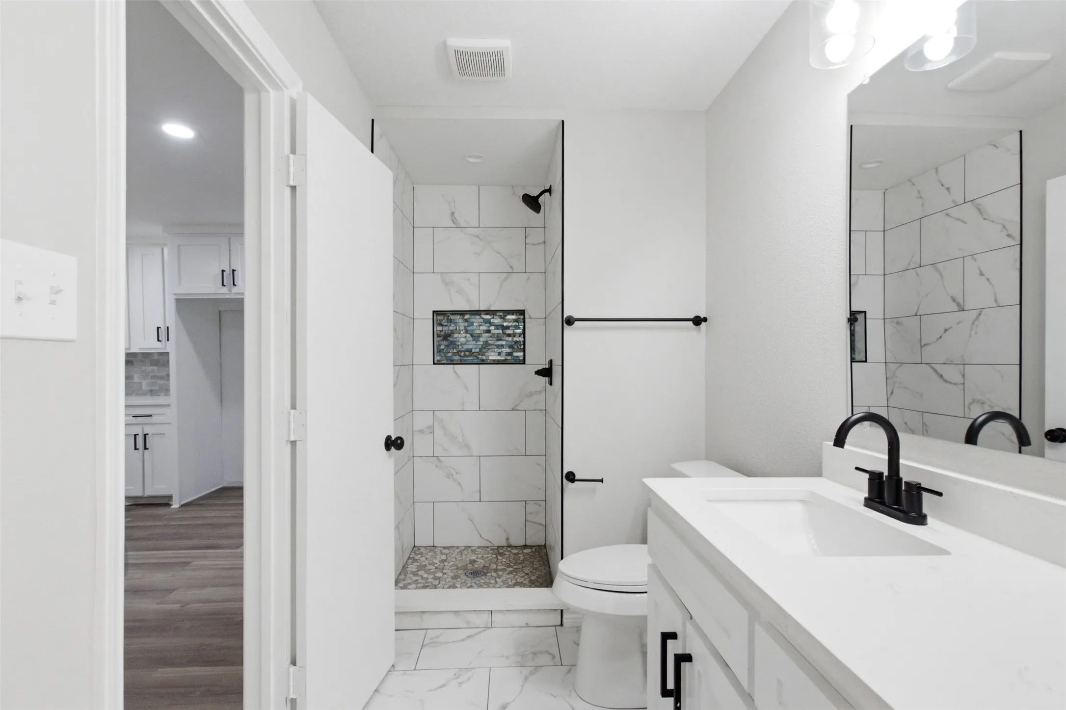 Bathroom featuring a walk-in shower with large format tile, a mosaic accent niche, and a stone pebble floor