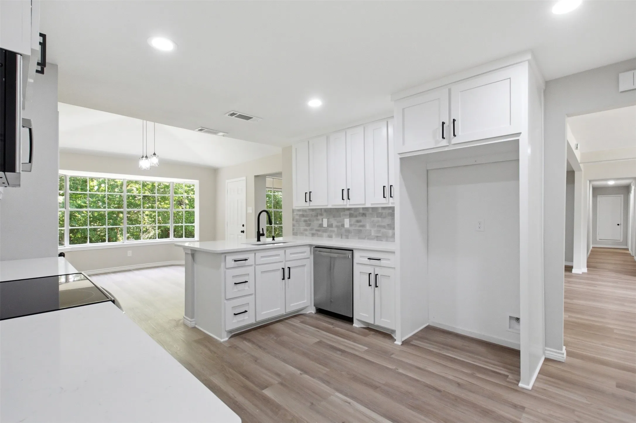 Modern kitchen featuring white shaker cabinetry, an island with a black faucet, stainless steel dishwasher, light wood-finish flooring, and a subway tile backsplash