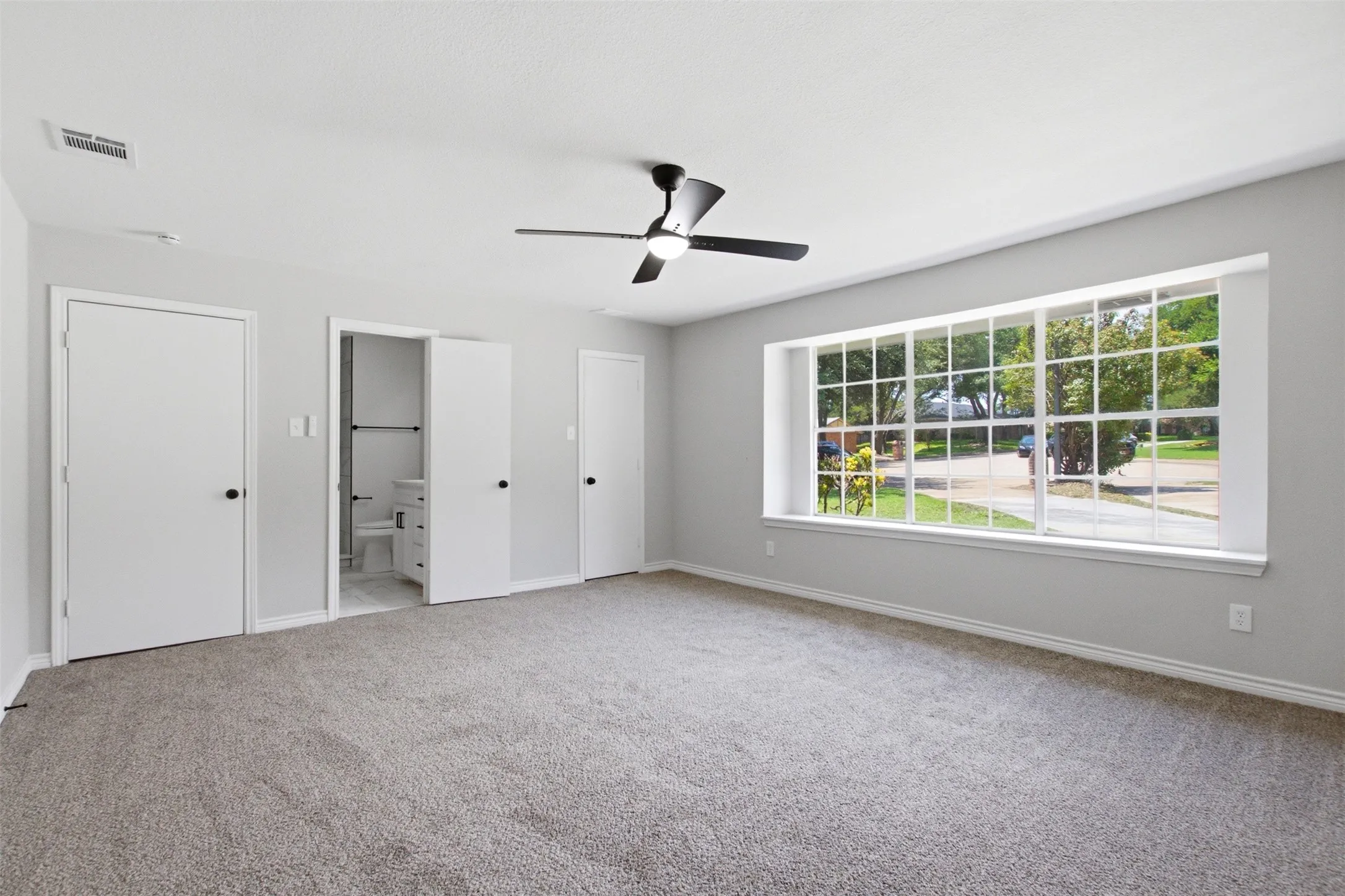 Spacious room featuring neutral carpeting, a black ceiling fan, and a large multi-pane window