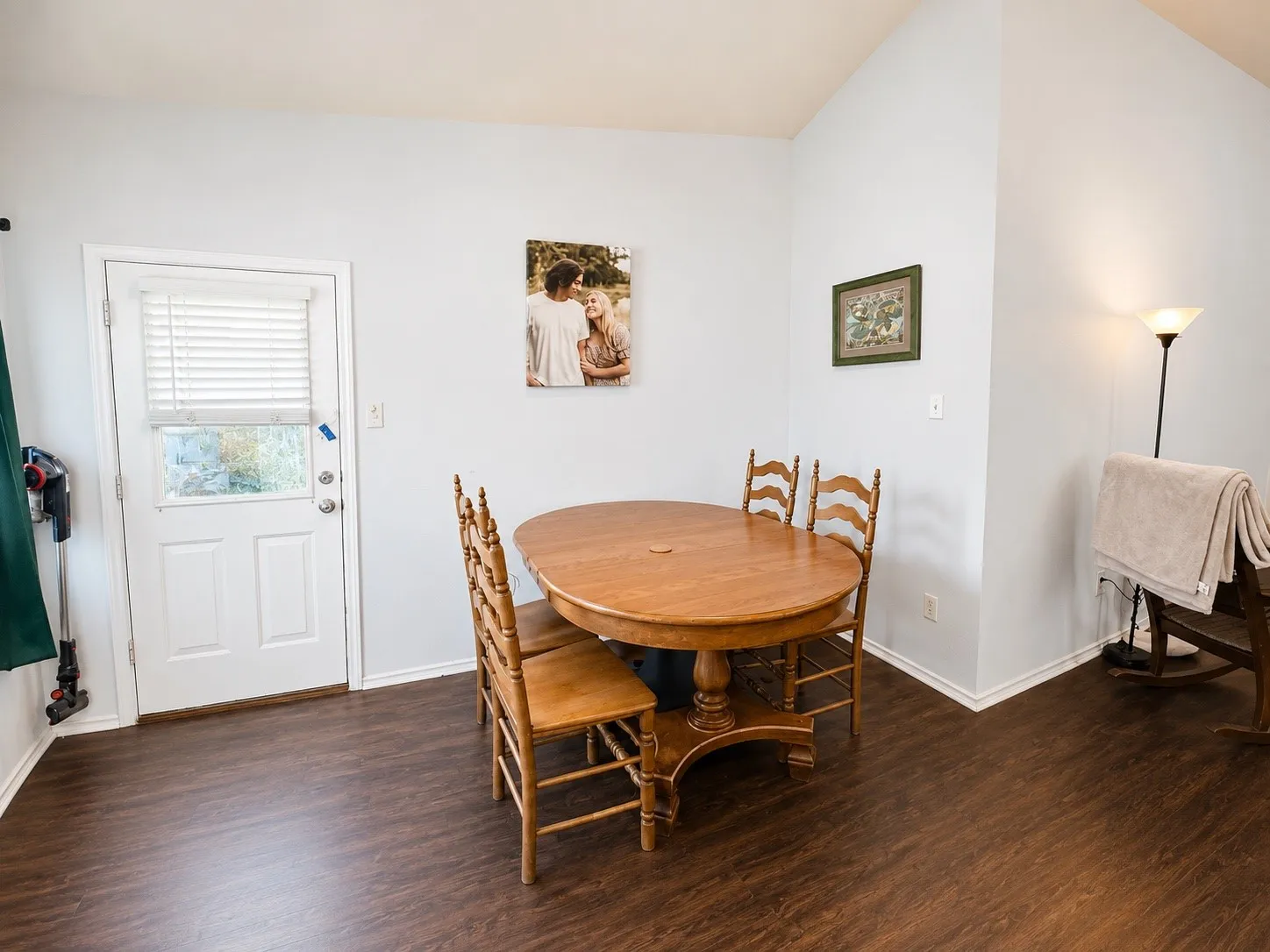 Spacious dining area featuring vaulted ceilings, wood-finish flooring, and a white paneled door with an integrated window blind