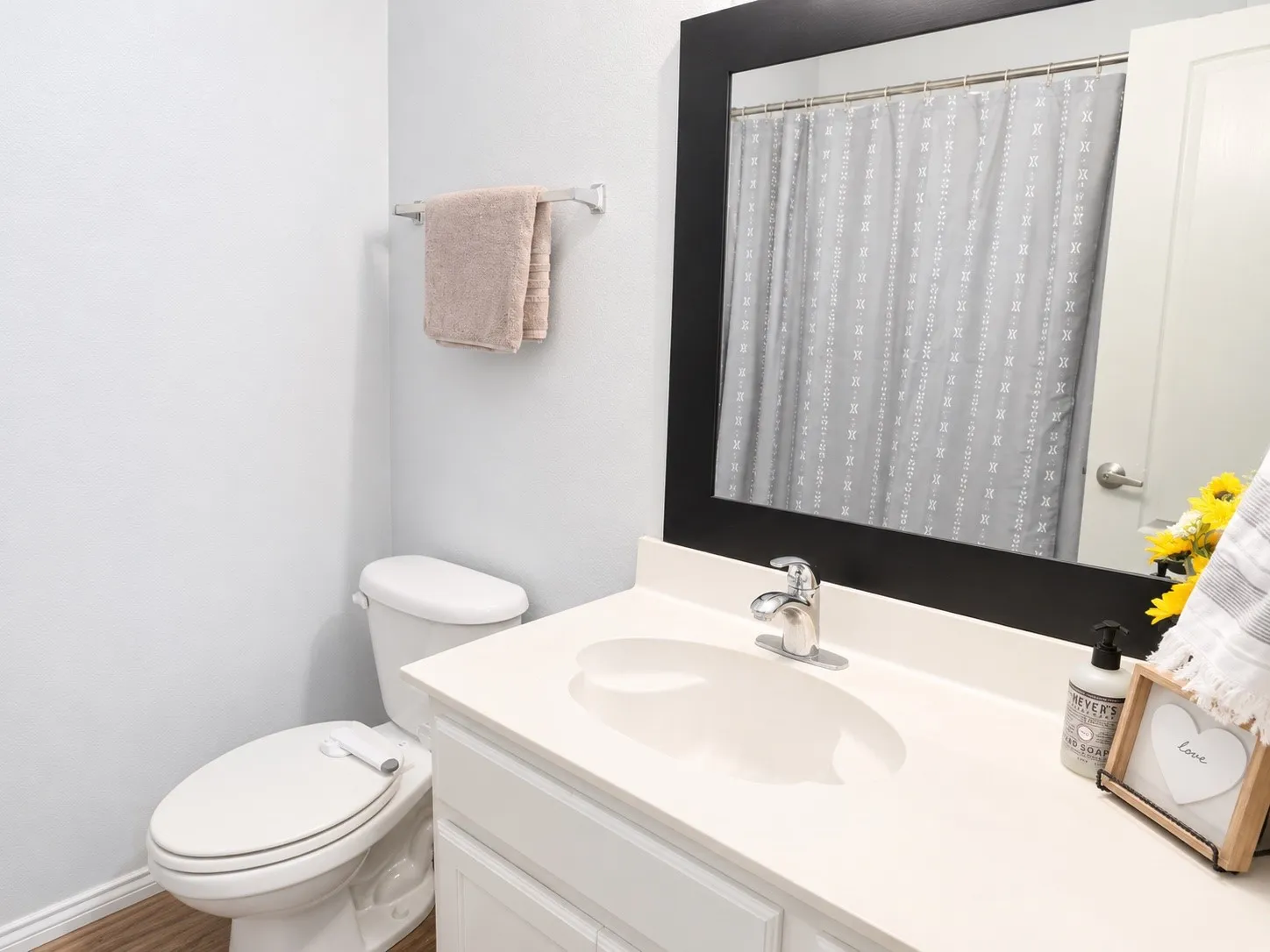 Bathroom featuring wood-finish flooring, a white vanity with an integrated sink, a chrome faucet, and a black framed mirror