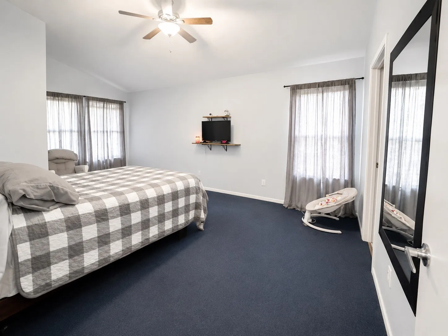 Spacious room featuring vaulted ceilings, a ceiling fan with integrated lighting, twin windows with curtain rods, and dark carpeting
