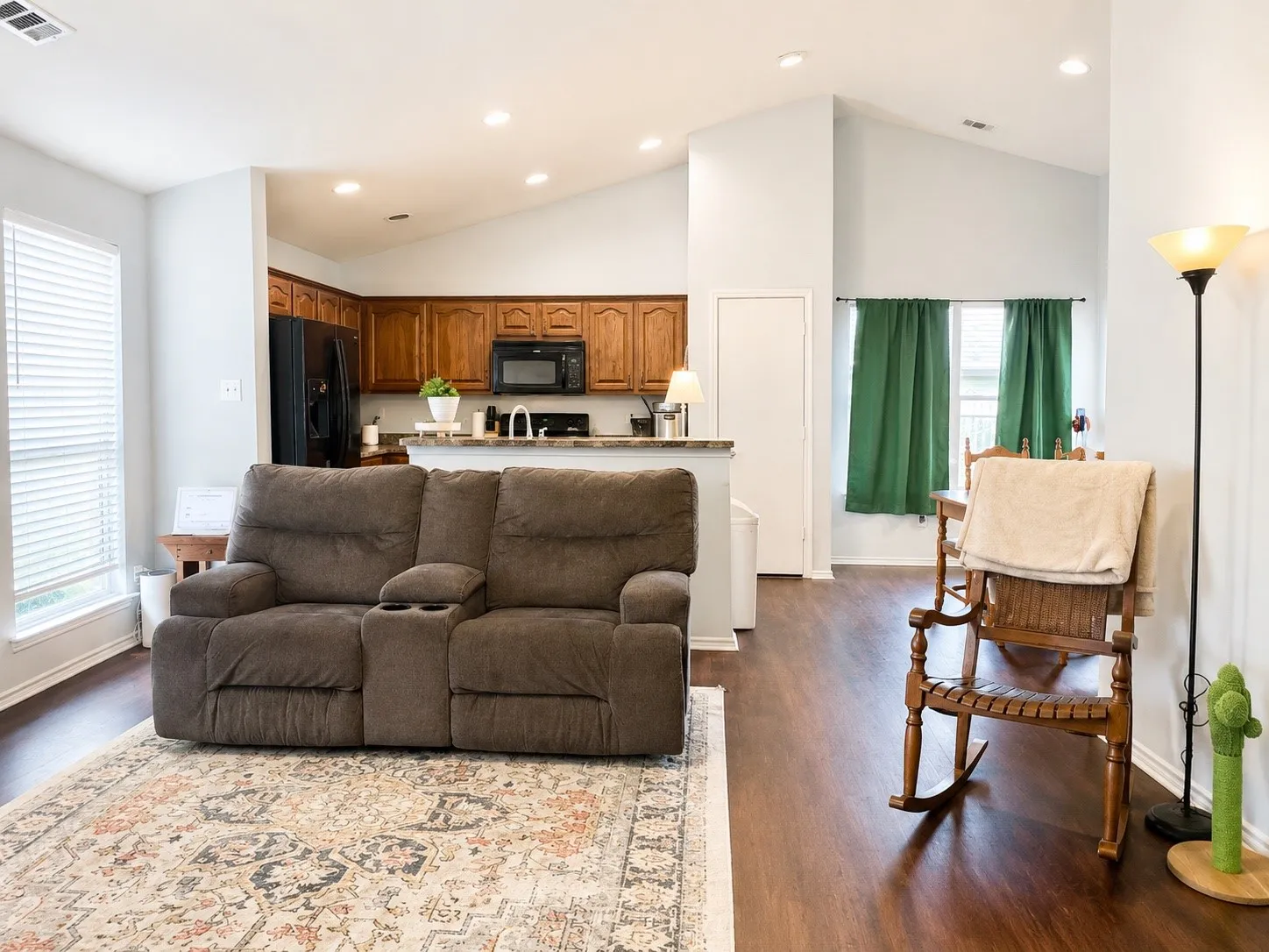 Spacious open-concept living area featuring wood-finish flooring, vaulted ceilings, and recessed lighting