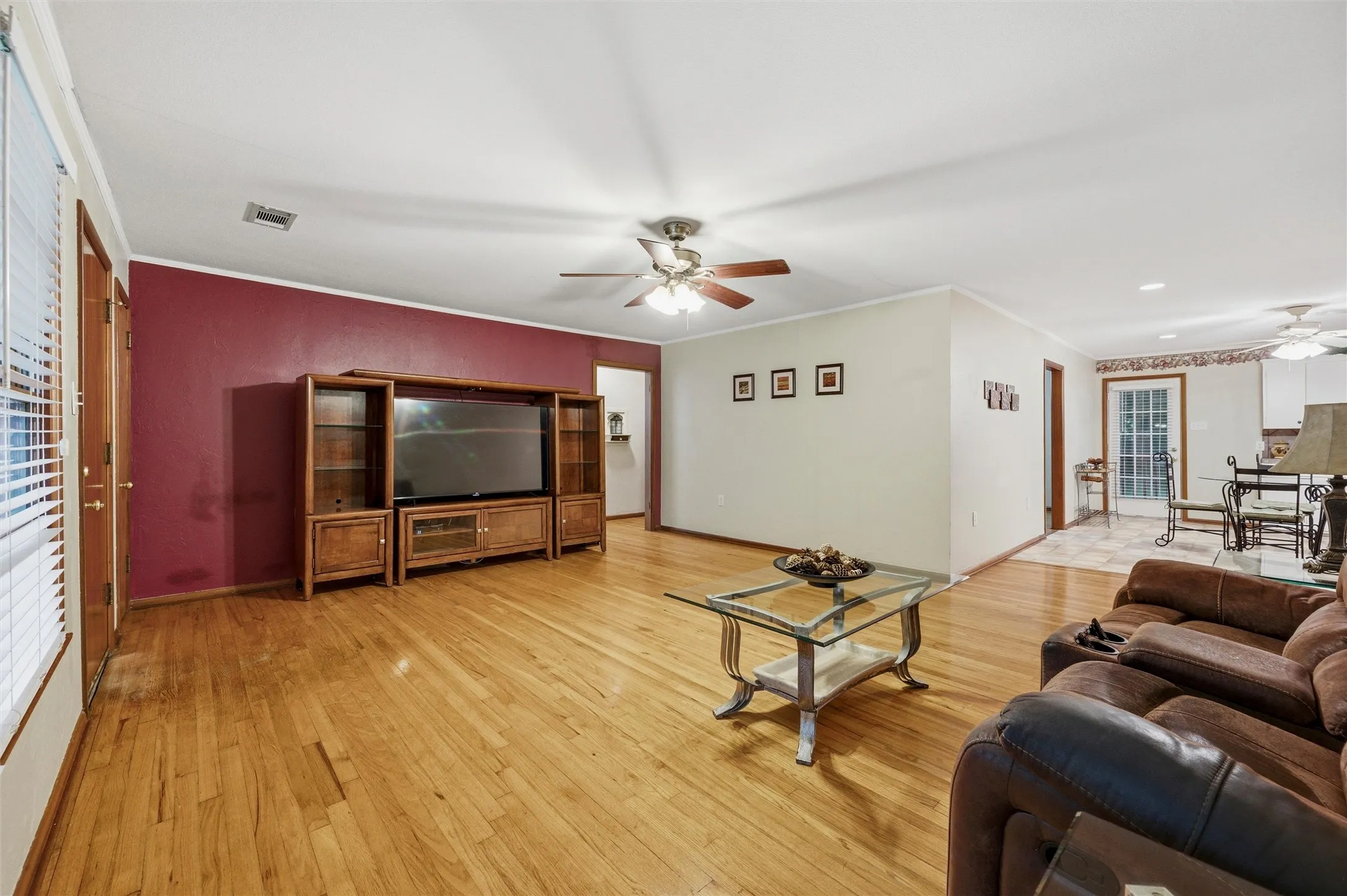 Living Room features crown molding and a ceiling fan with light fixture. Open layout connects directly to the eat-in kitchen. Deep red accent wall is visible from the main living area. Hardwood flooring extends throughout.