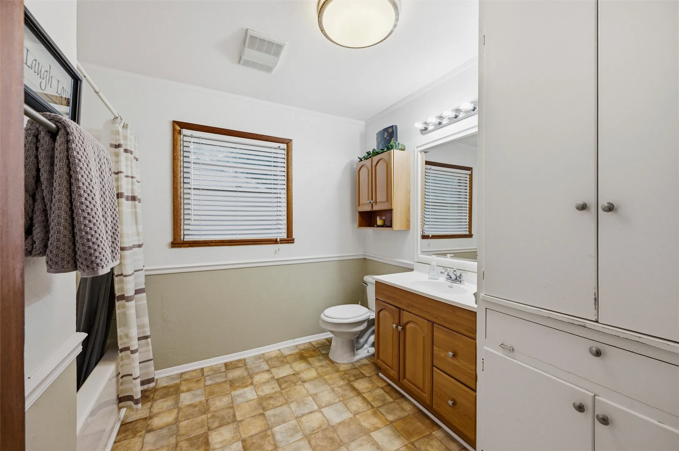 Bathroom features a single-sink vanity with wood cabinetry and framed mirror. Wall cabinet provides additional storage. Window provides natural light. Tile flooring extends throughout.