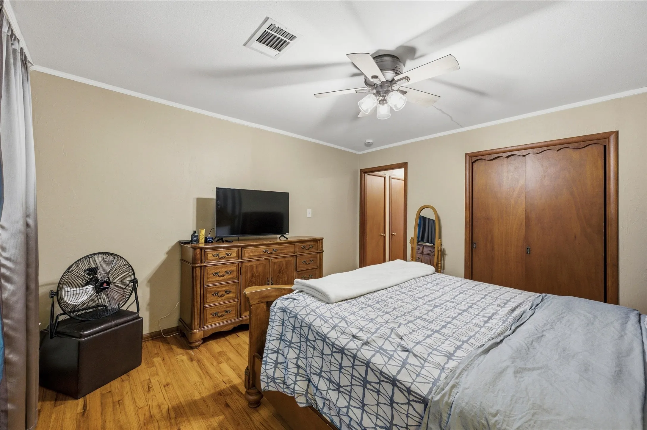 Primary Bedroom features crown molding and a ceiling fan with light fixture. Double closet doors provide ample storage. Doorway connects directly to the hallway. Hardwood flooring extends throughout.