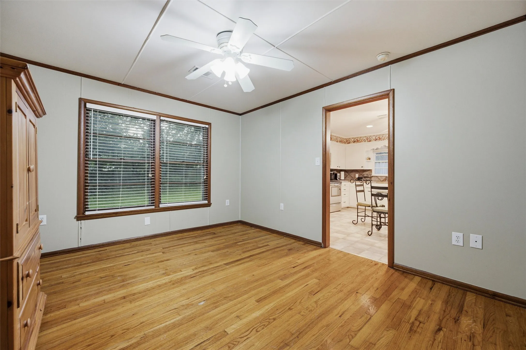 Secondary Bedroom features crown molding and a ceiling fan with light fixture. Two windows provide front-facing natural light. Blue two-tone accent walls with decorative border are visible throughout. Hardwood flooring extends throughout.