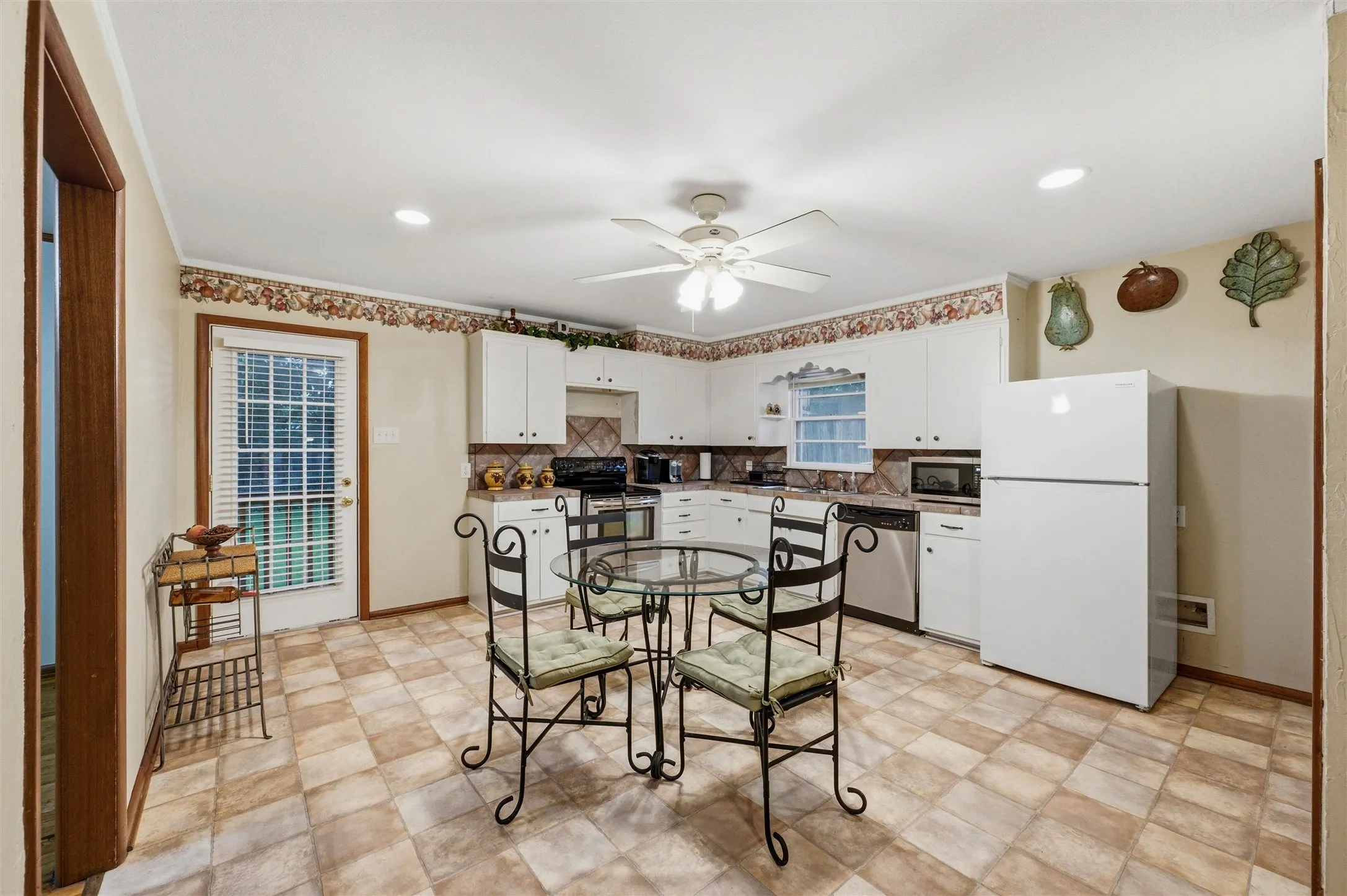 Eat-In Kitchen features recessed lighting and a ceiling fan with light fixture. Rear exterior door provides backyard access and natural light. Open layout connects directly to the kitchen. Tile flooring extends throughout.
