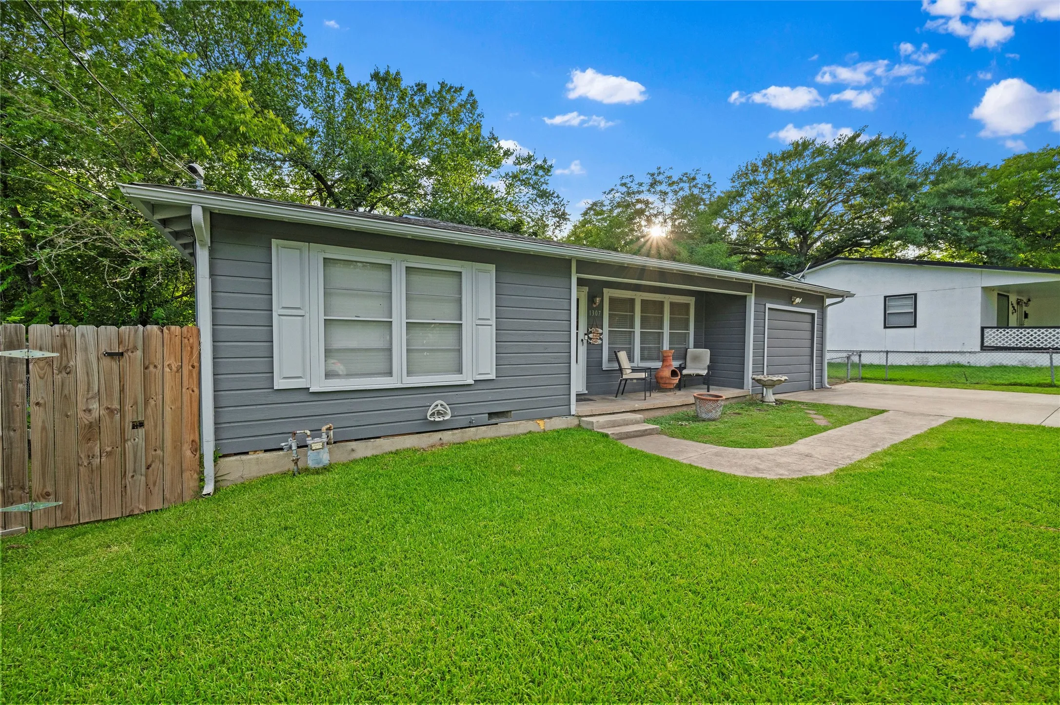 Front Exterior features gray lap siding accented by white trim and shutters. Covered front porch spans the entry. Wood privacy fencing borders the left side of the property.
