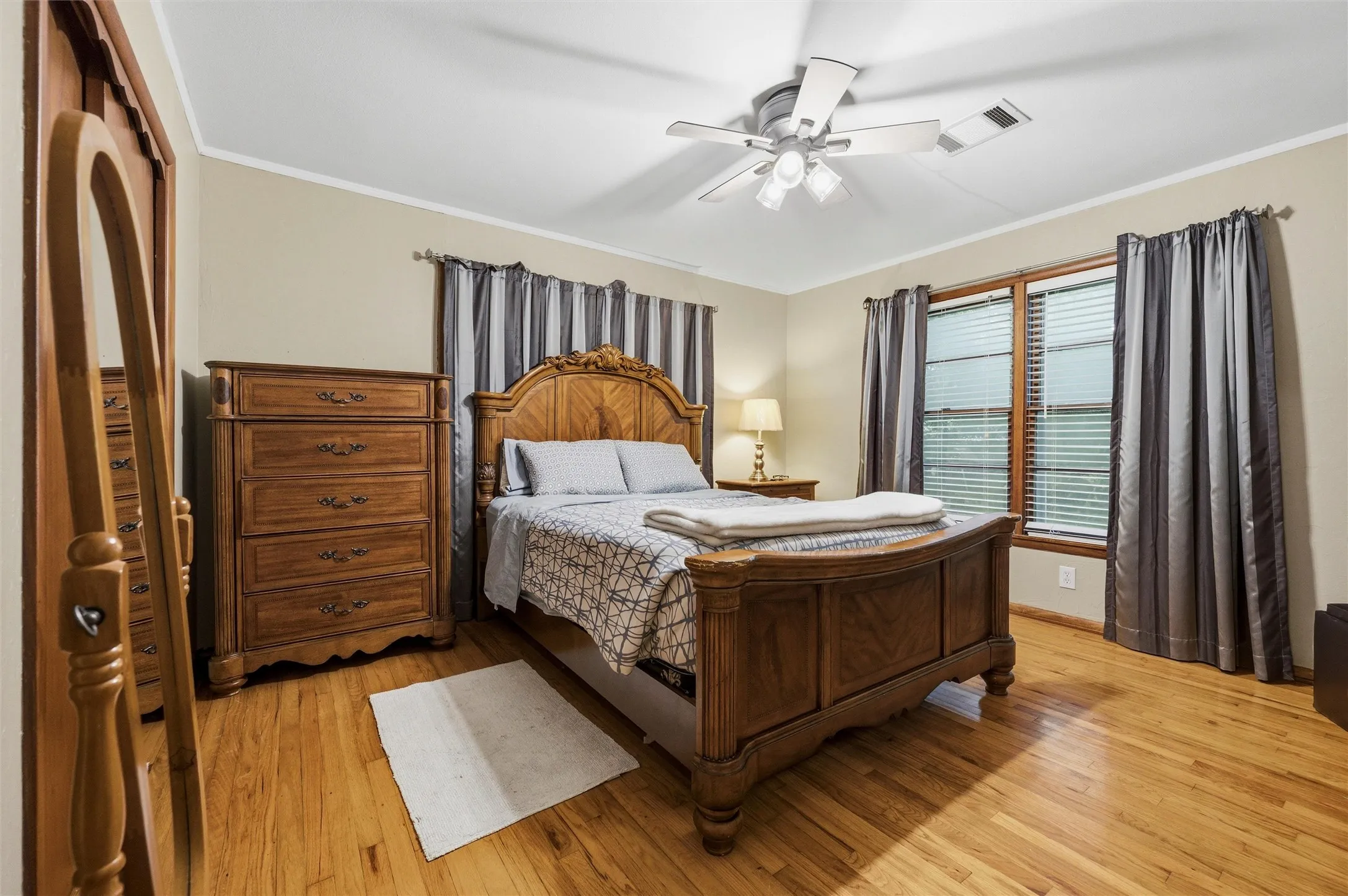 Primary Bedroom features crown molding and a ceiling fan with light fixture. Window provides natural light throughout the room. Hardwood flooring extends throughout.