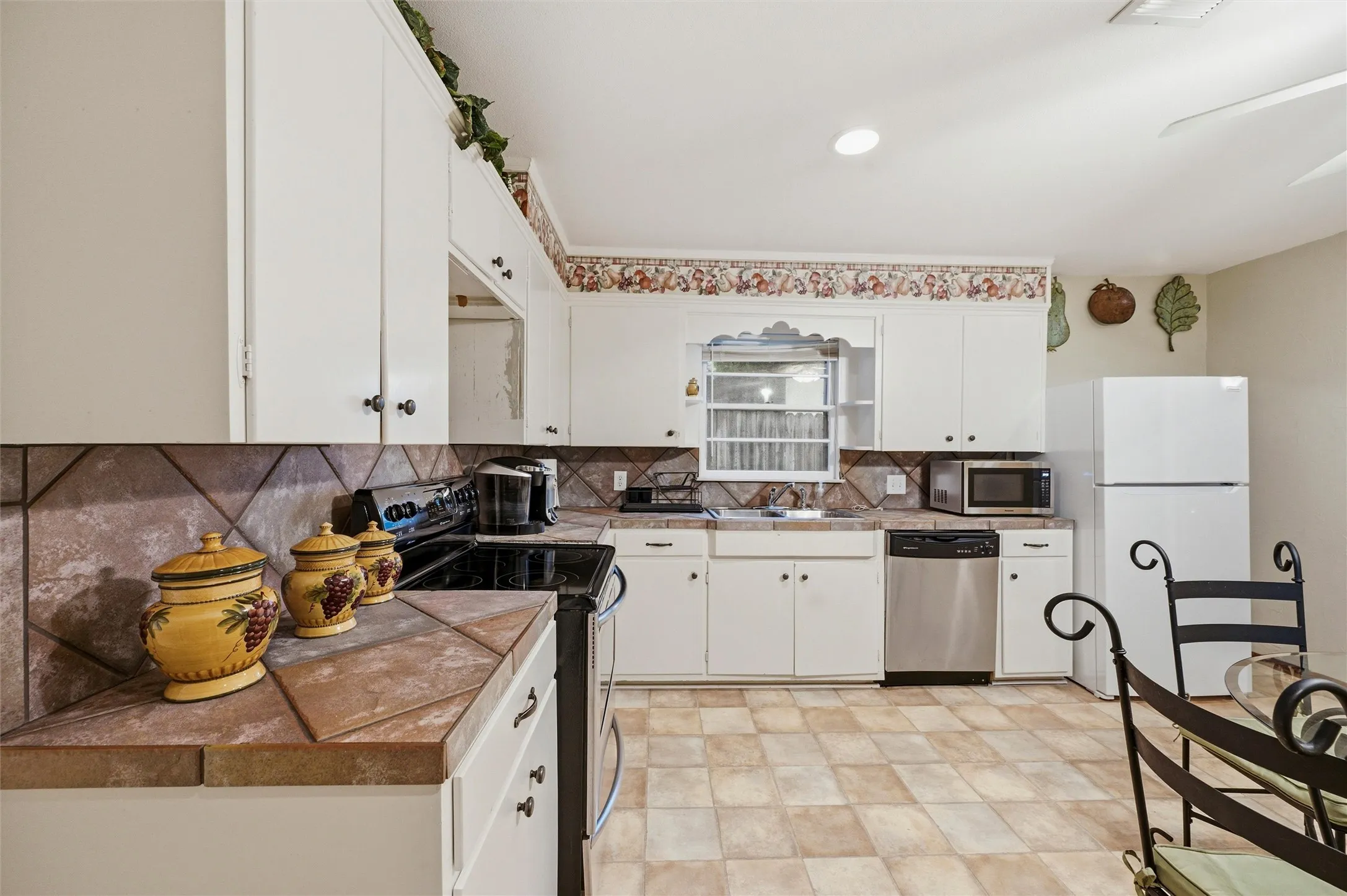 Kitchen features white raised-panel cabinetry and generous counter space. Stainless steel appliances and double sink provide everyday functionality. Eat-in dining area is visible adjacent to the kitchen. Tile flooring extends throughout.
