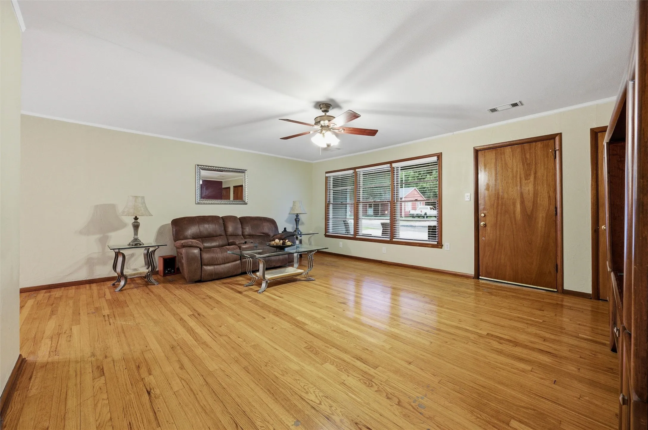 Living Room features crown molding and a ceiling fan with light fixture. Large picture window overlooks the front yard. Wood interior door provides front entry access. Hardwood flooring extends throughout.