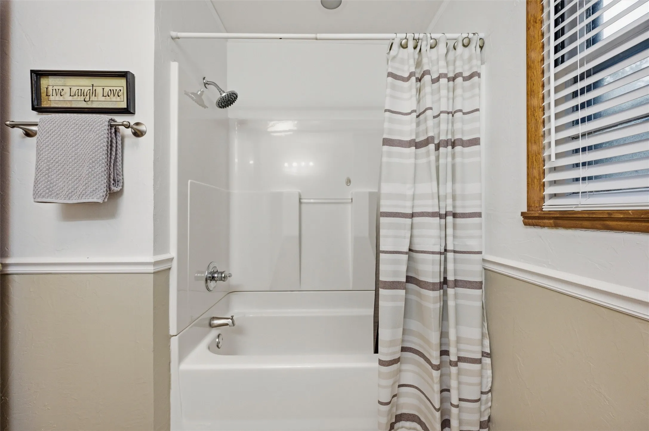Bathroom features a white tub and shower combination with chrome fixtures. Window provides natural light. Chair rail molding accents the walls. Tile flooring extends throughout.