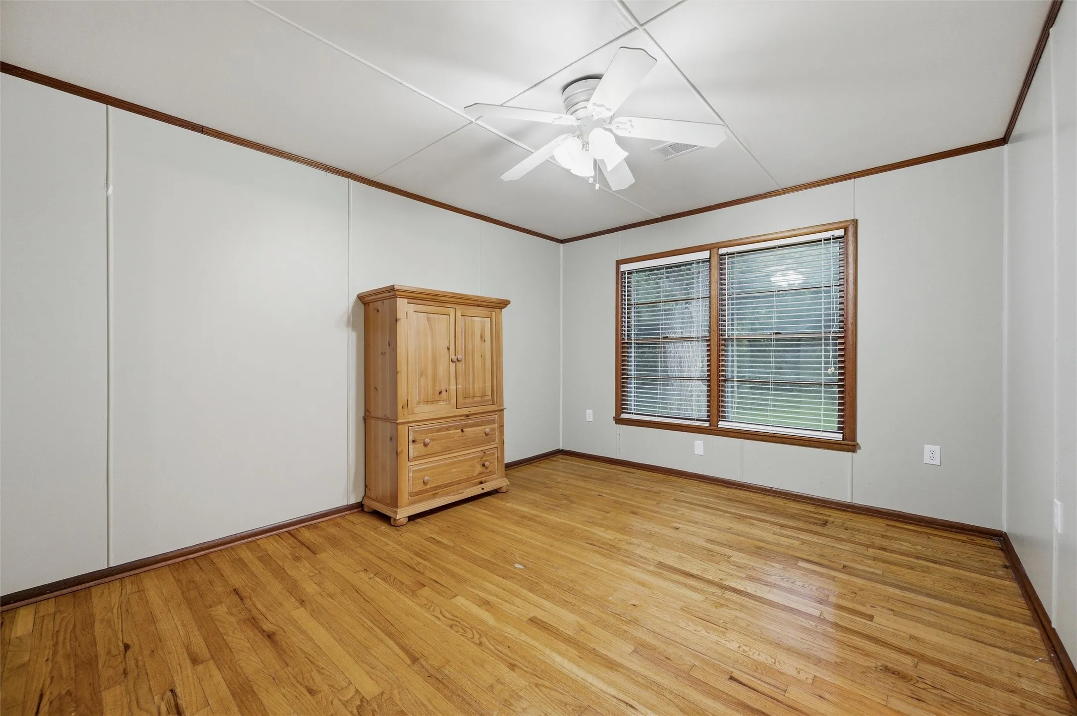 Secondary Bedroom features crown molding and a ceiling fan with light fixture. Window provides natural light. Closet door provides storage. Hardwood flooring extends throughout.