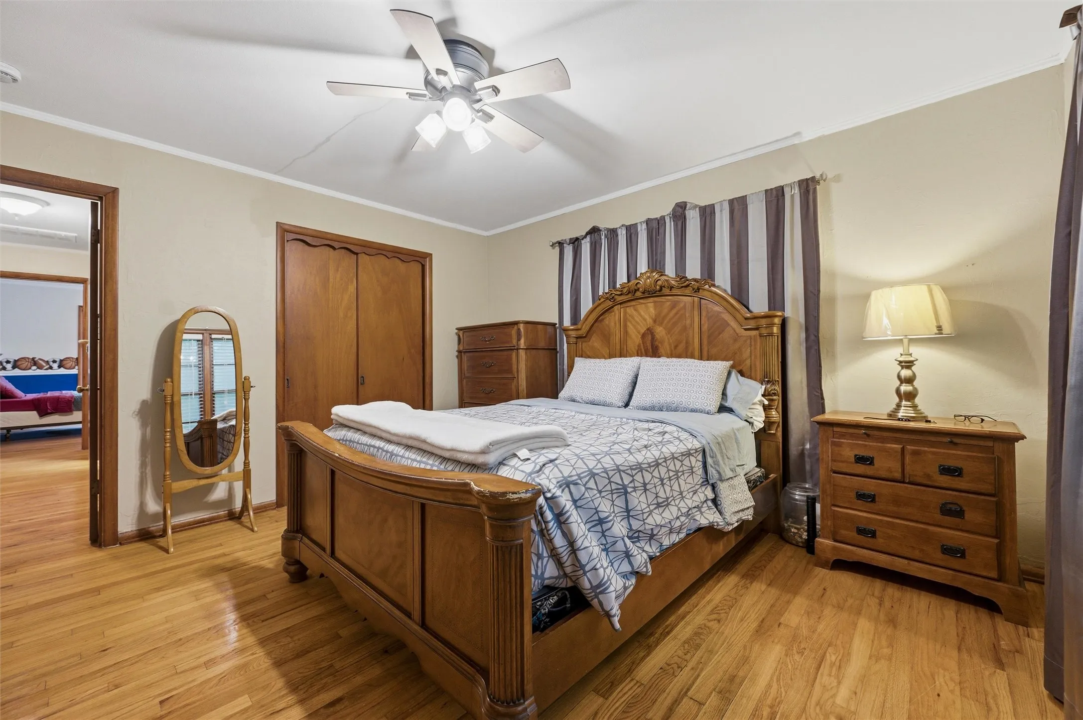 Primary Bedroom features crown molding and a ceiling fan with light fixture. Double closet doors provide storage. Open doorway connects directly to the living area. Hardwood flooring extends throughout.