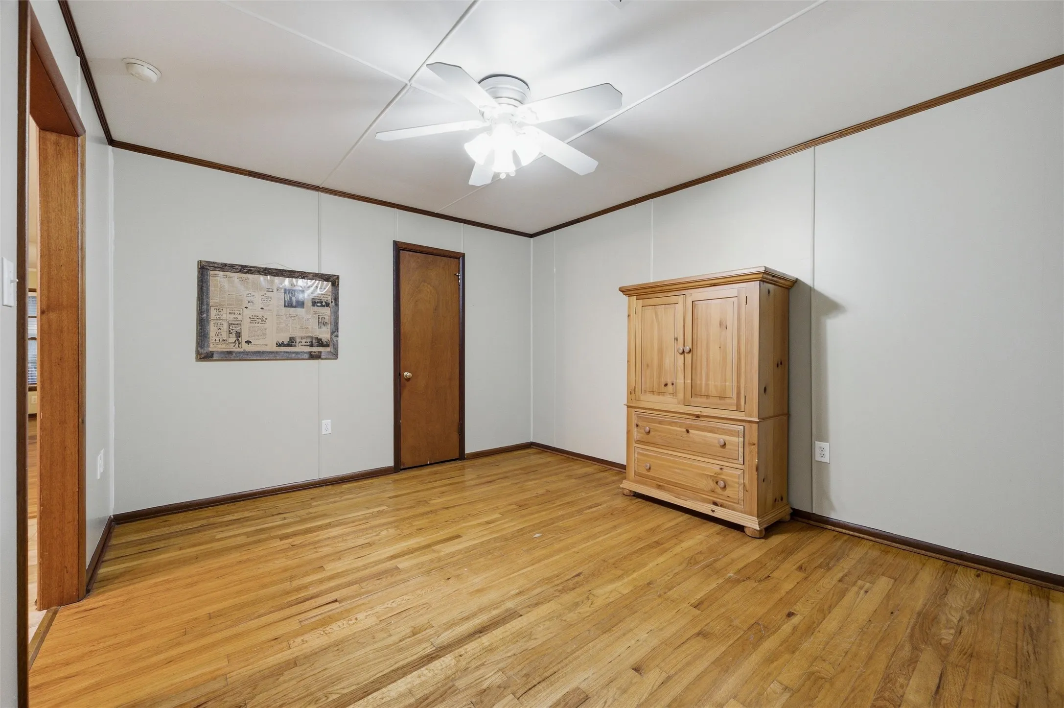 Secondary Bedroom features crown molding and a ceiling fan with light fixture. Double windows provide natural light. Closet door provides storage access. Doorway connects directly to the hallway. Hardwood flooring extends throughout.