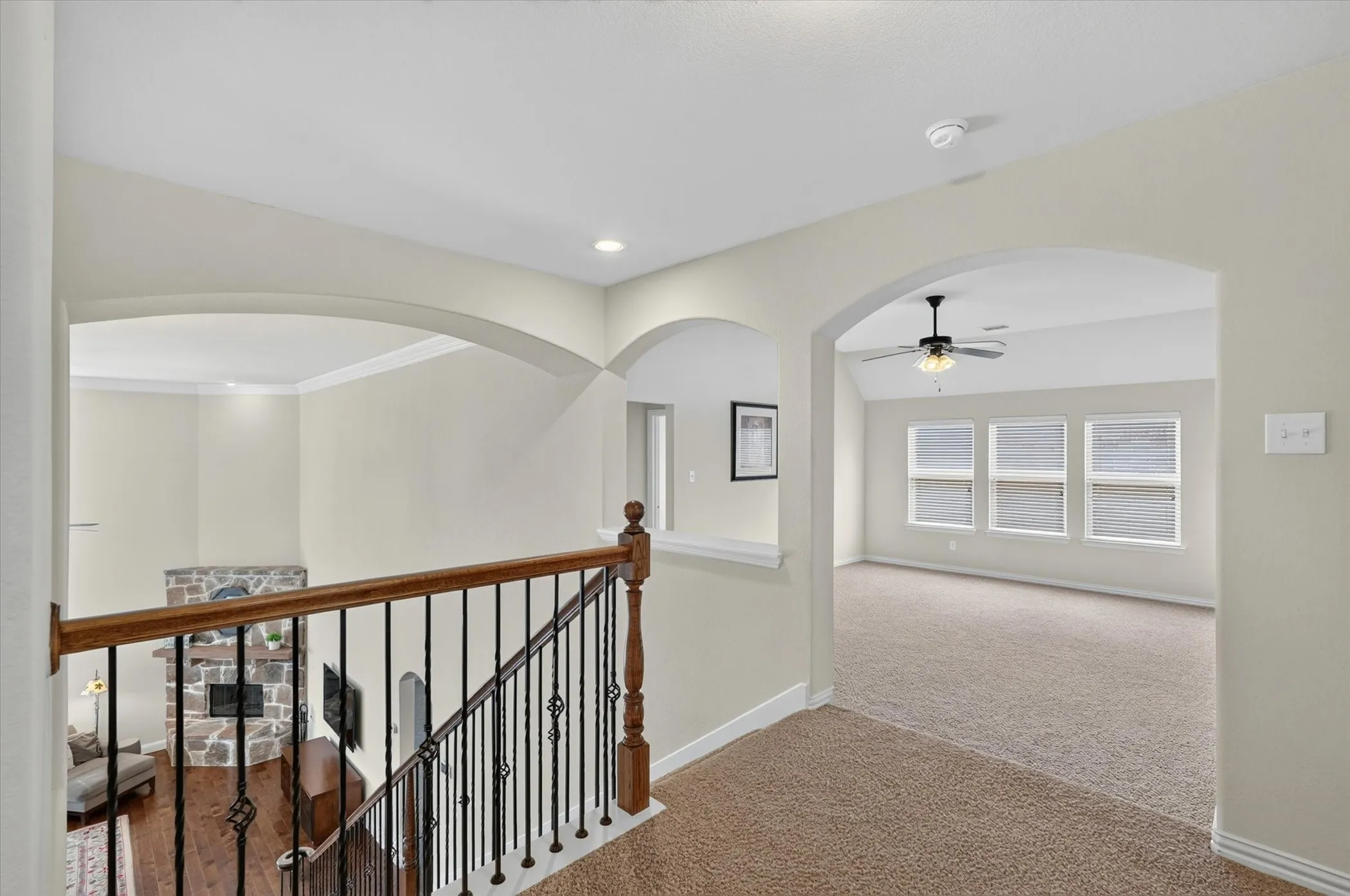 Spacious upper landing with arched doorways, warm neutral wall tones, carpeted flooring, and a decorative iron and wood staircase railing