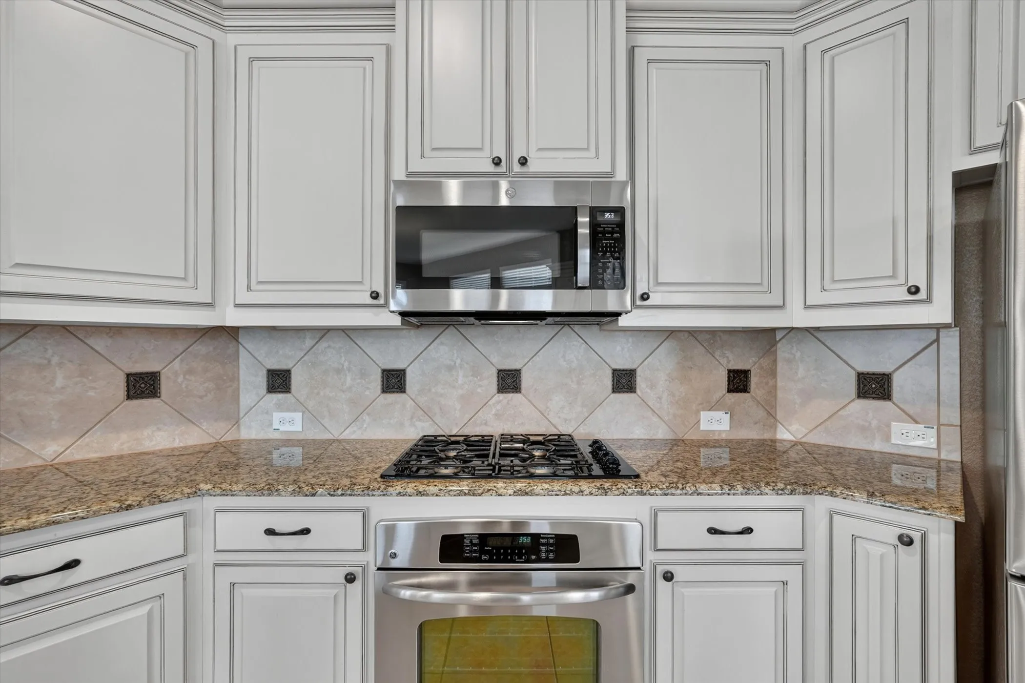 Kitchen featuring light-toned cabinetry, stainless steel appliances, granite countertops, and a decorative tile backsplash