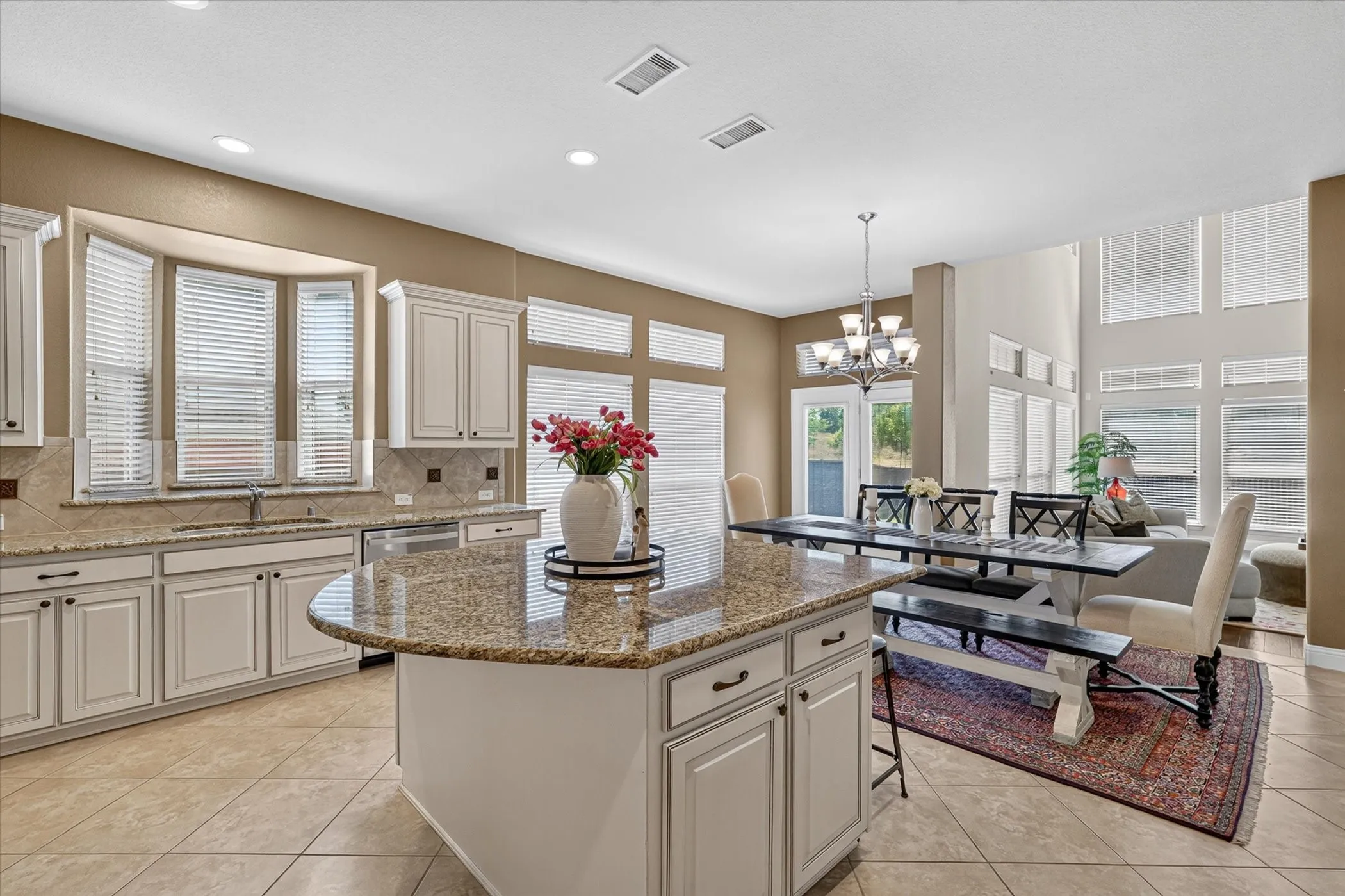 Kitchen with a large island featuring a granite countertop, white cabinetry with dark hardware, and a bay window over the sink