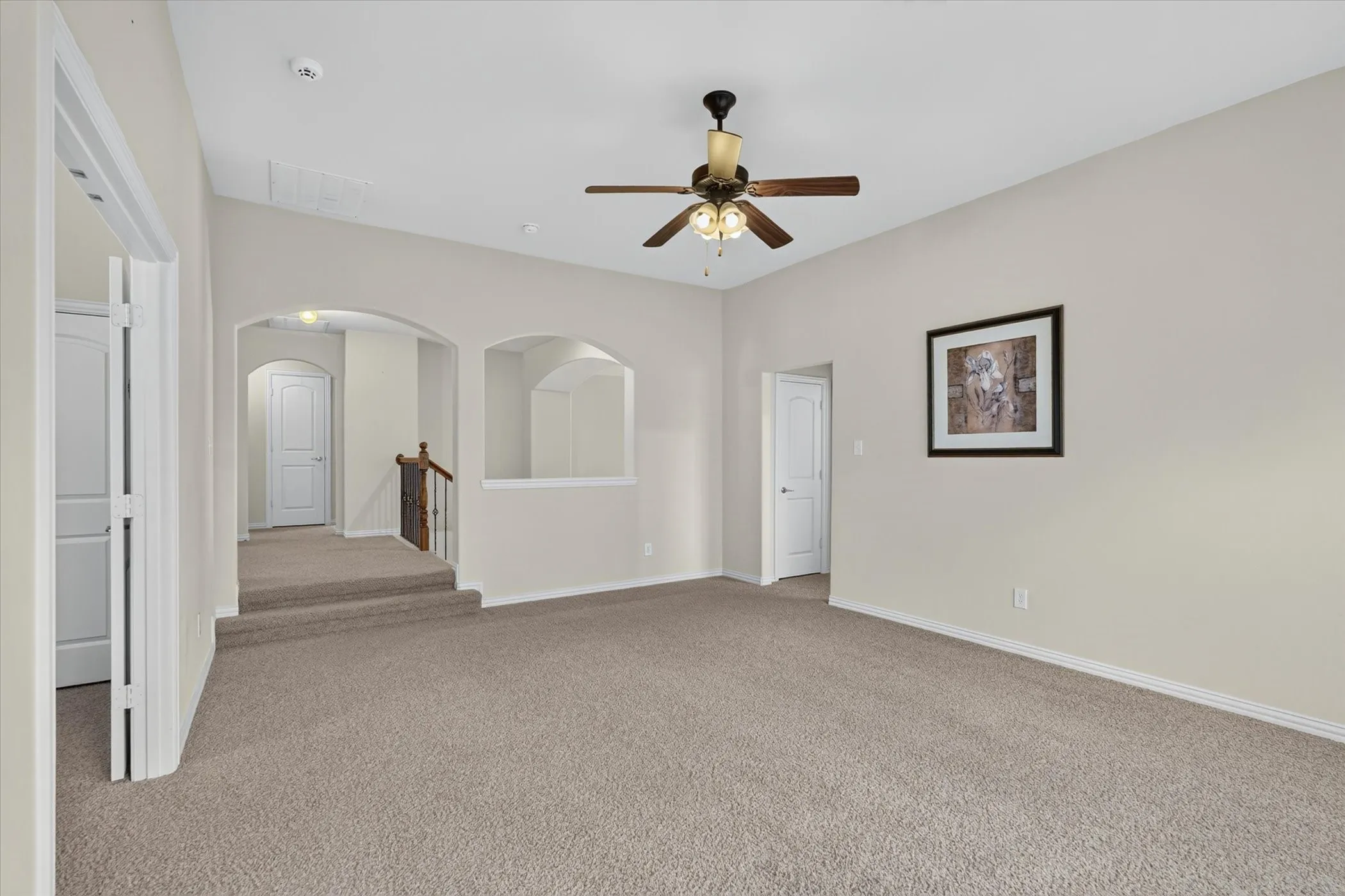 Carpeted landing area featuring a ceiling fan, arched doorways, a built-in architectural niche, and a wooden handrail