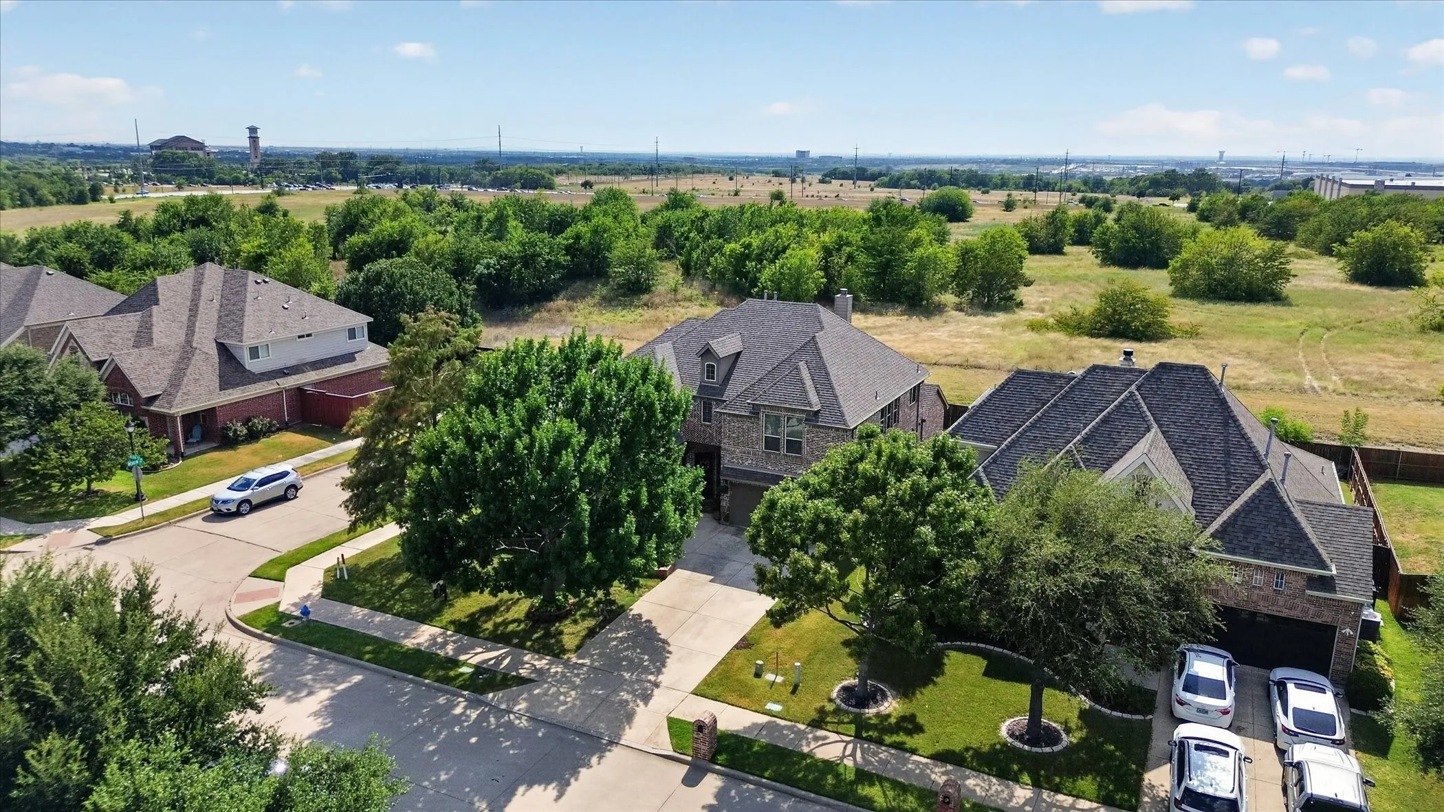 Residential property featuring a brick and stone exterior, dark shingle roof, attached garage, concrete driveway, and established landscaping