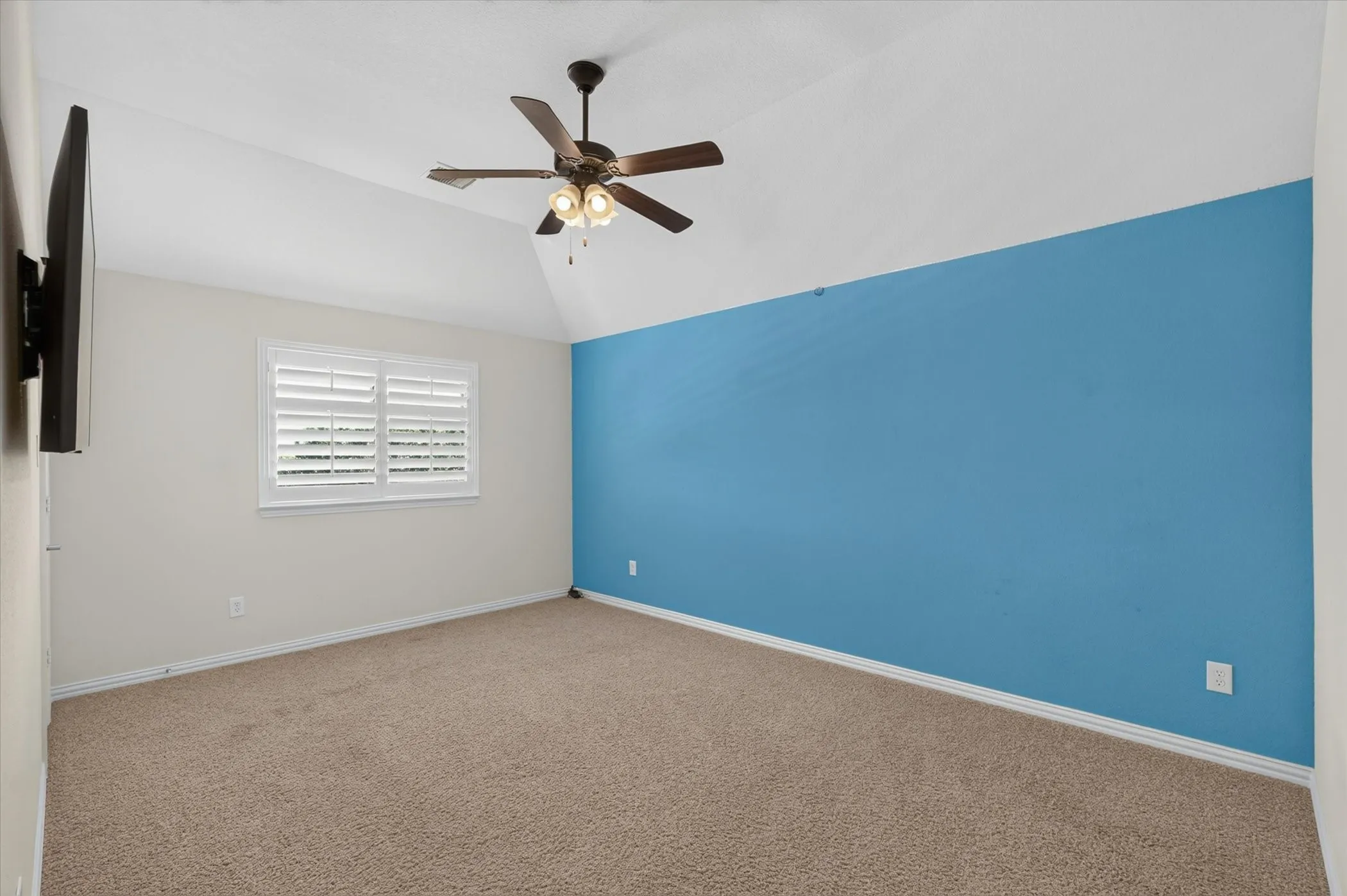 Room featuring vaulted ceilings, plush carpeting, a single window with plantation shutters, a partial accent wall, and a ceiling fan with integrated lighting