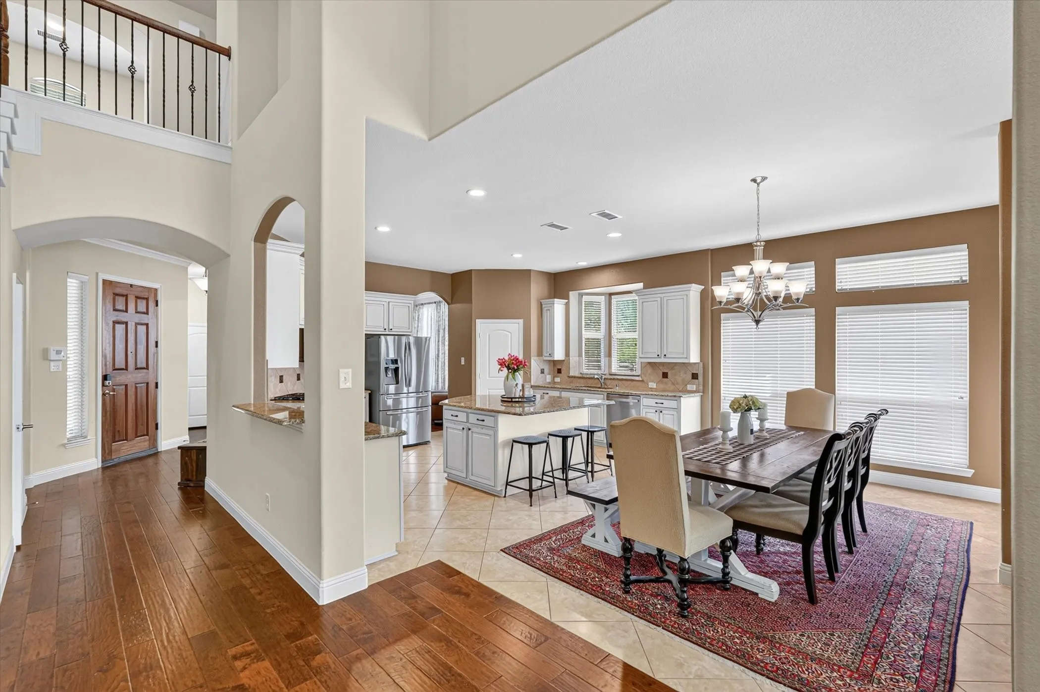Open-concept living space featuring wood-finish flooring, a two-story foyer with a wrought iron railing, and a kitchen with white cabinetry and a central island