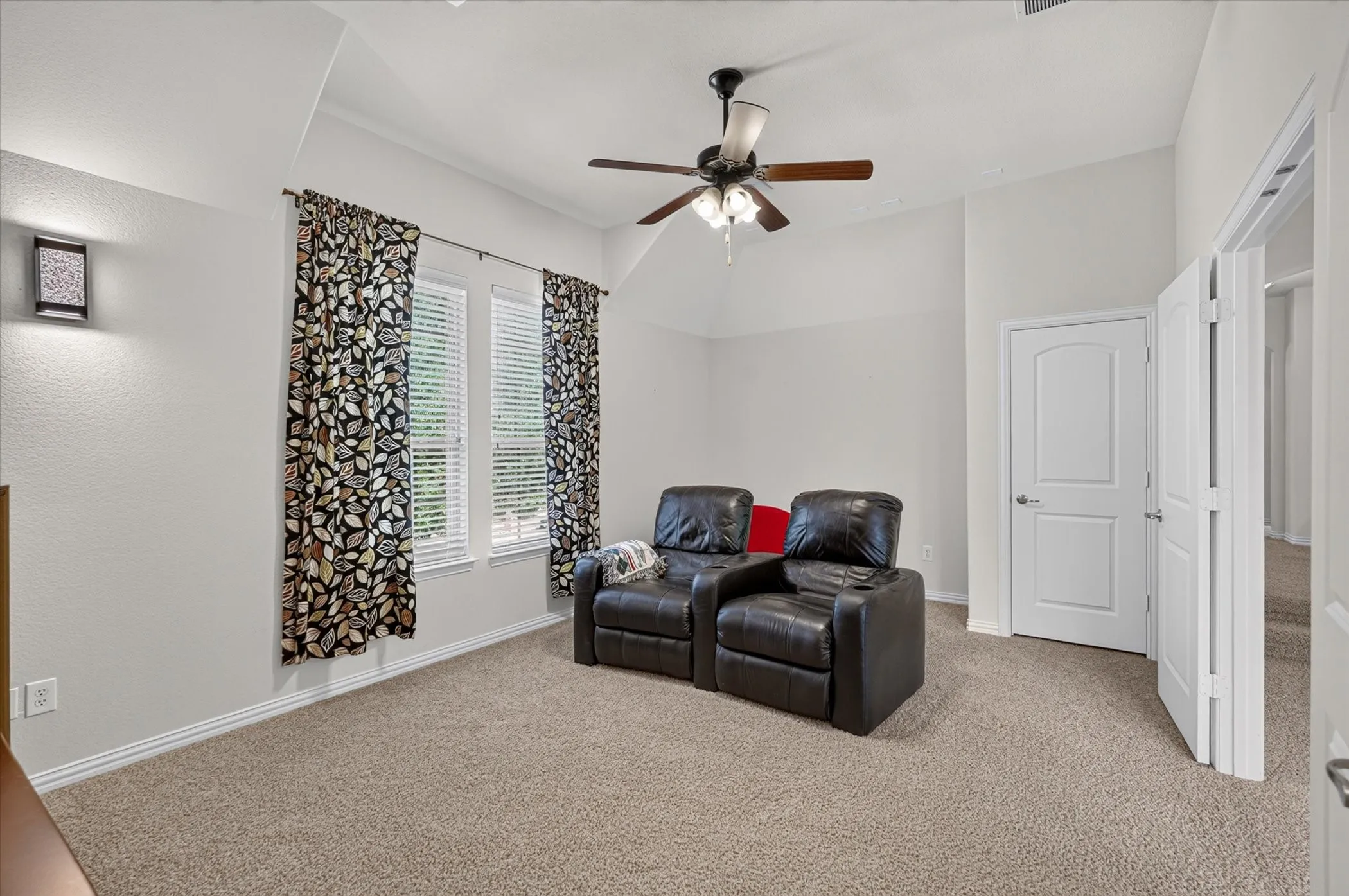 Carpeted room featuring a ceiling fan, dual windows with blinds, a wall sconce, and white paneled doors