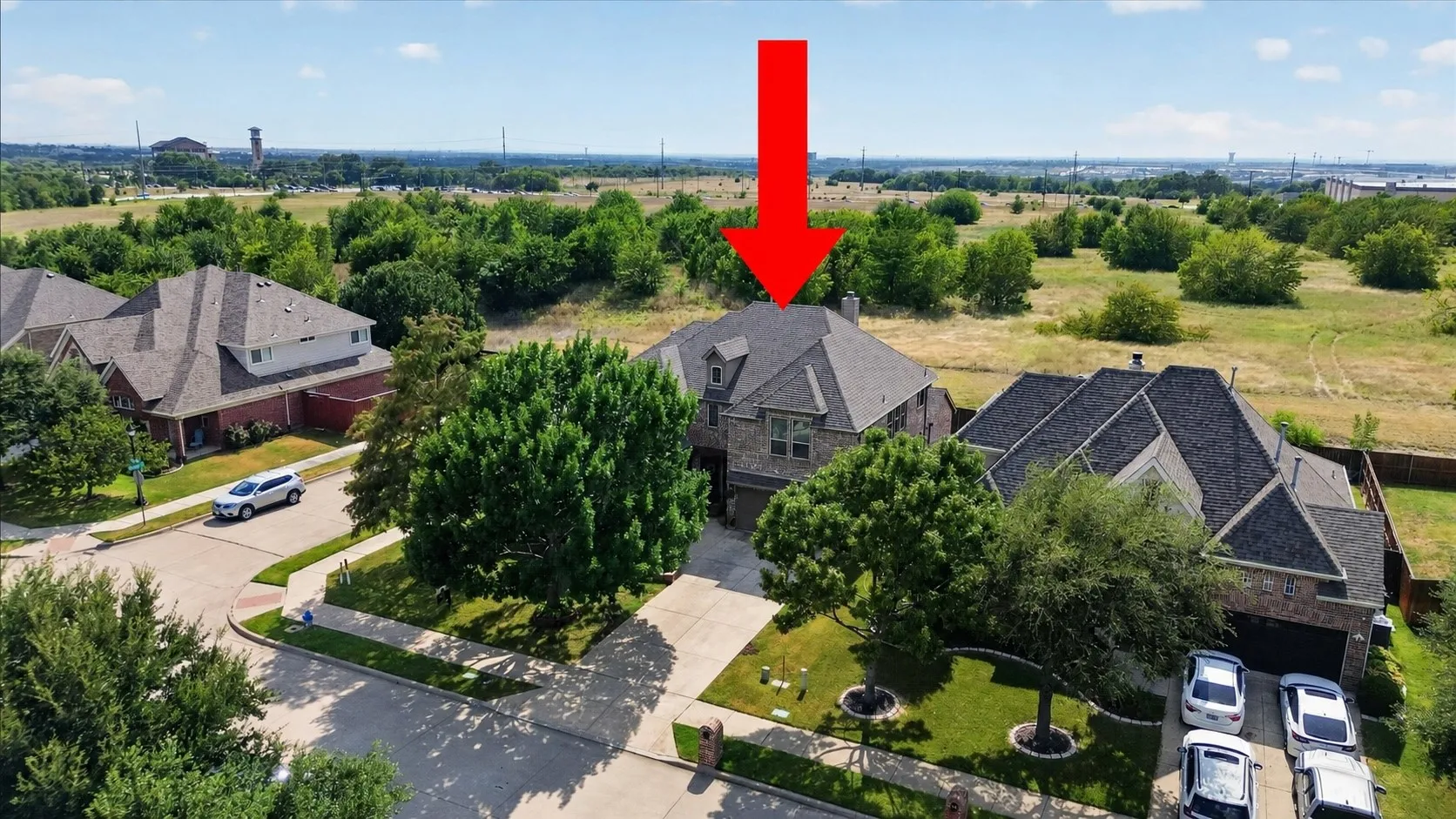 Stone and brick facade residence with a multi-gabled roofline, mature front yard trees, a concrete driveway, and an attached garage