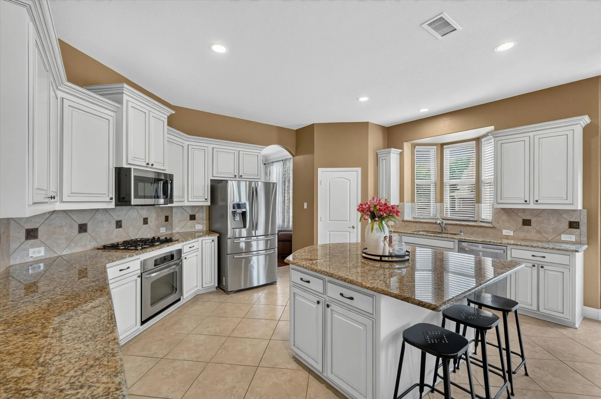 Spacious kitchen featuring white cabinetry, granite countertops, stainless steel appliances, a tiled backsplash, and a central island with seating