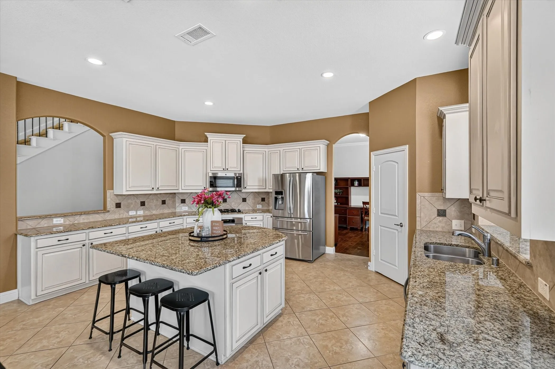 Expansive kitchen featuring a large central island, light-toned cabinetry, stainless steel appliances, granite countertops, and tile flooring