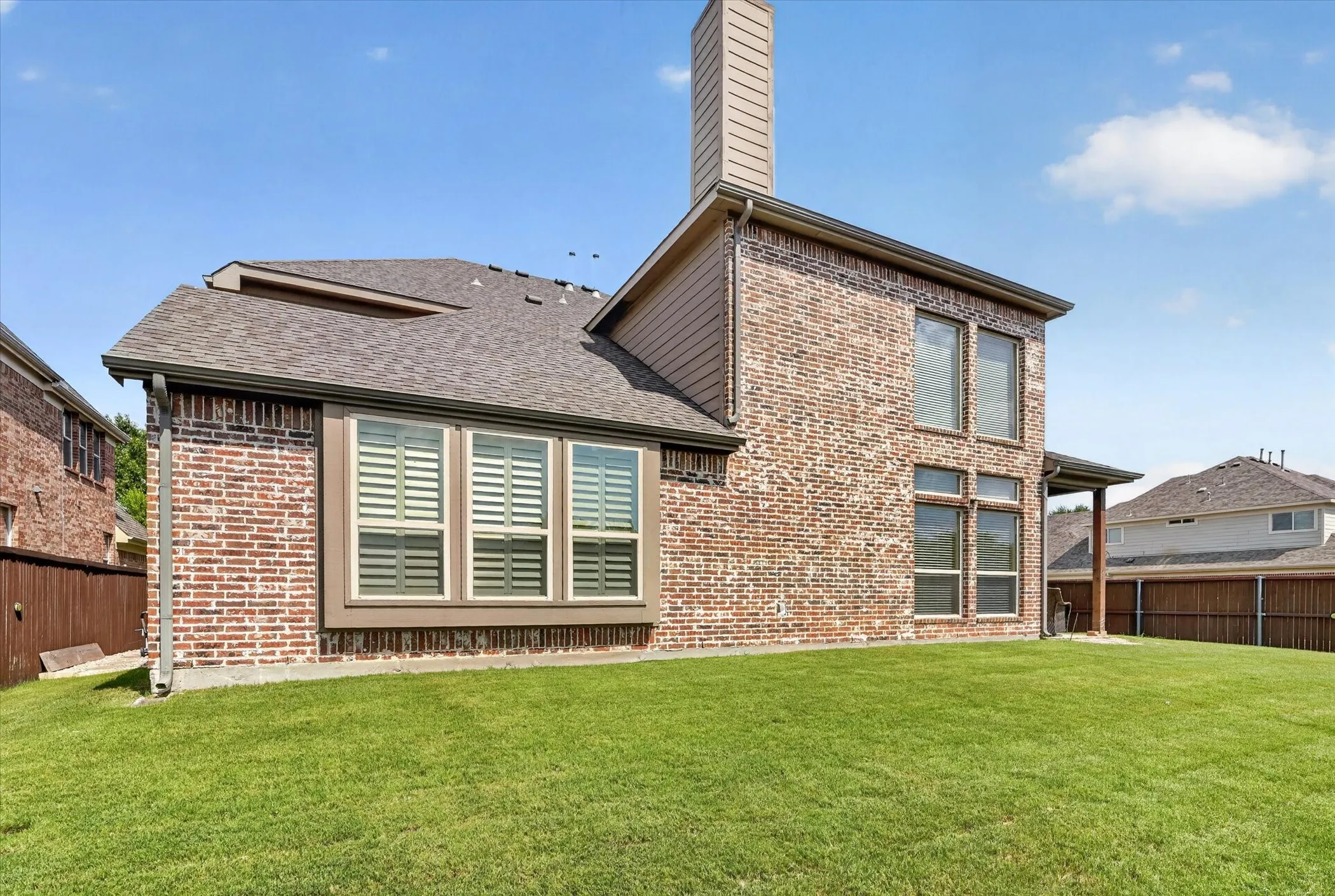 Brick exterior featuring a covered patio, multiple windows with blinds, and a prominent chimney
