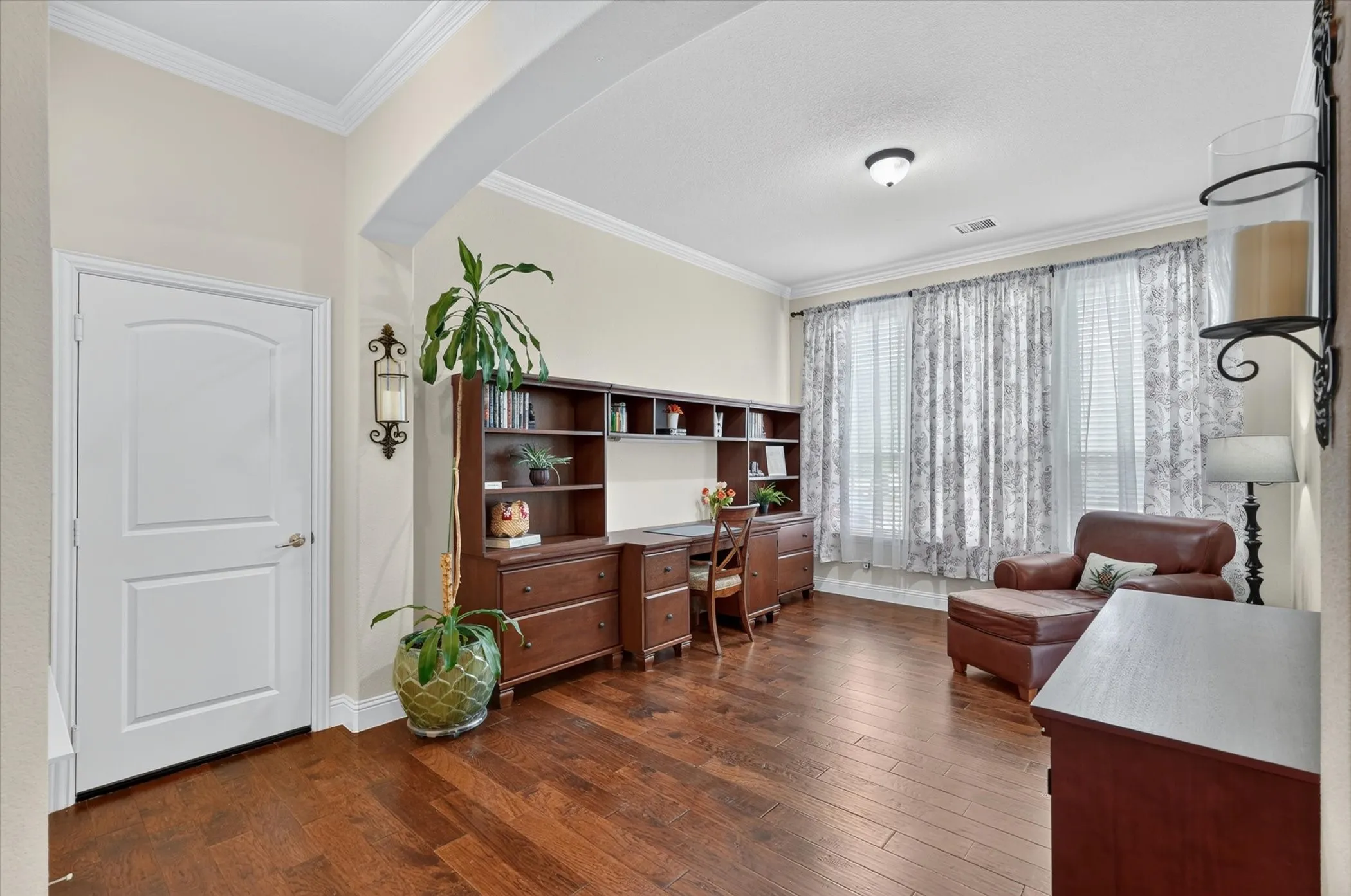 Spacious room featuring rich wood-finish flooring, an arched entryway, and crown molding