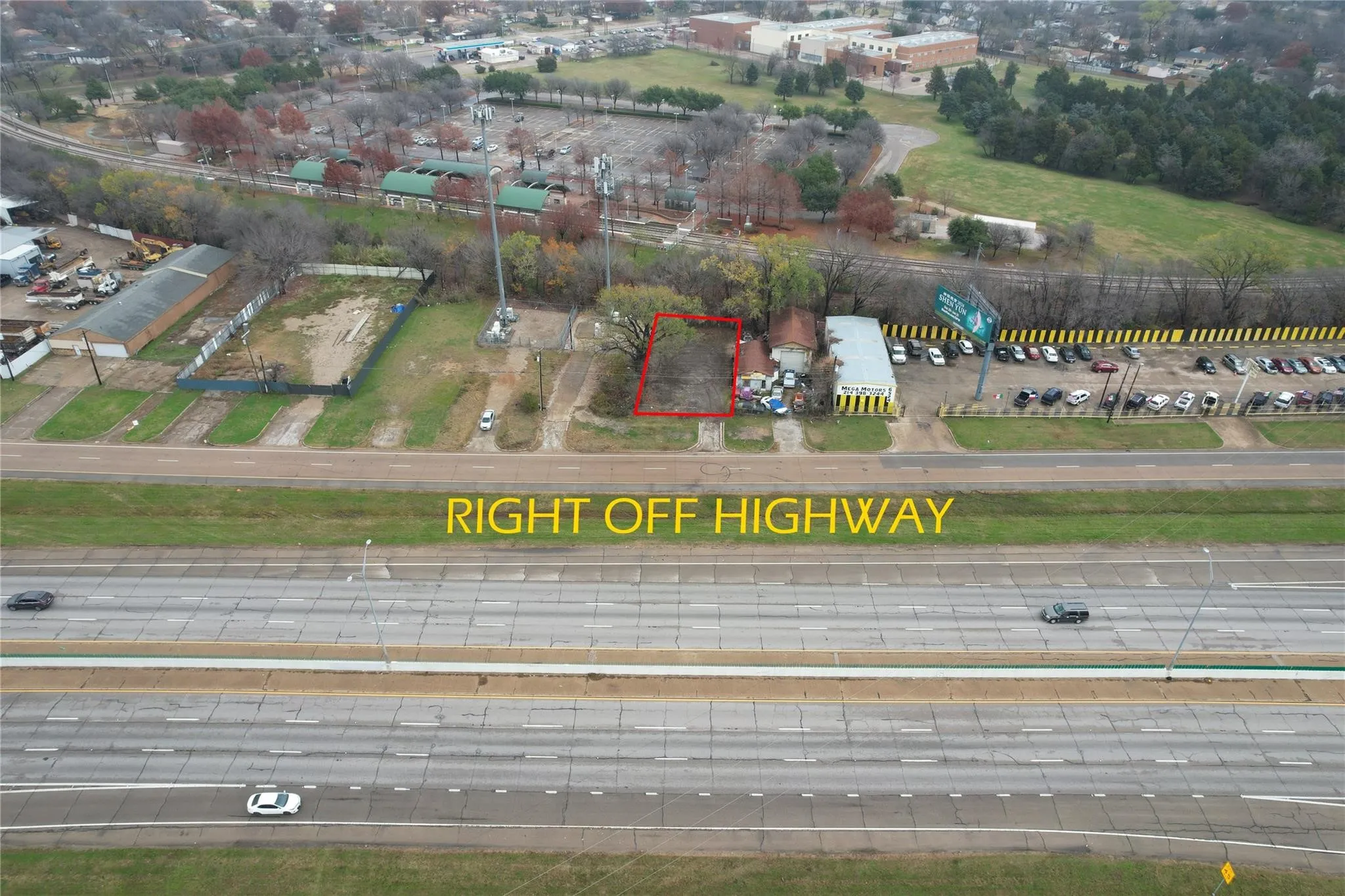 Aerial perspective showcasing a vacant parcel of land, clearly outlined in red, positioned directly adjacent to a multi-lane highway