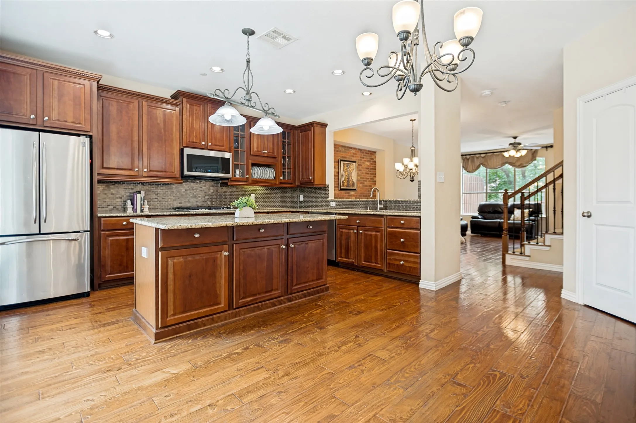 Kitchen featuring wood-finish flooring, dark wood cabinetry, stainless steel appliances, granite countertops, and a central island with pendant lighting