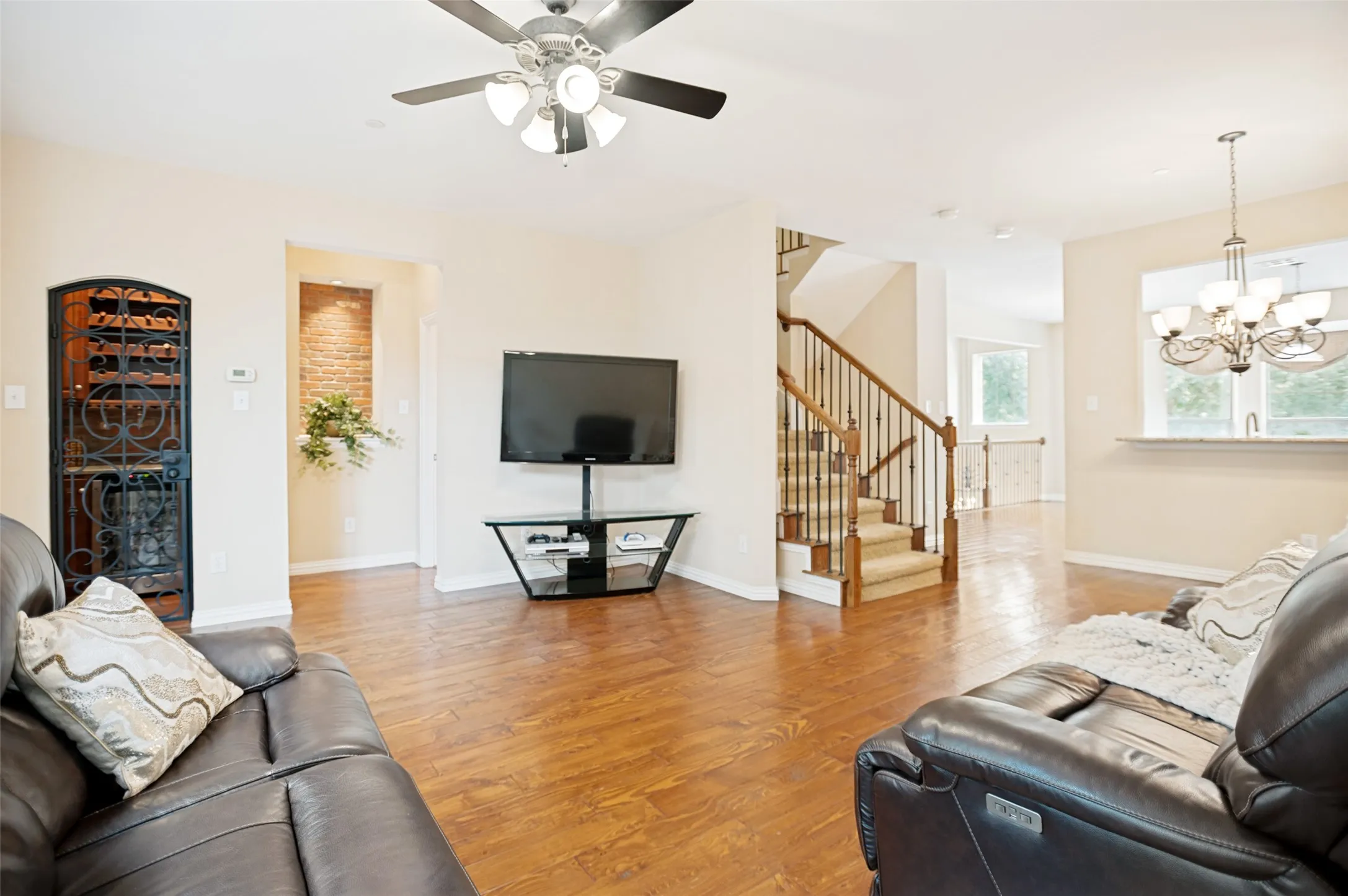 Open-concept living area featuring wood-finish flooring, a built-in wine rack with an ornate metal door, and a brick-accented niche