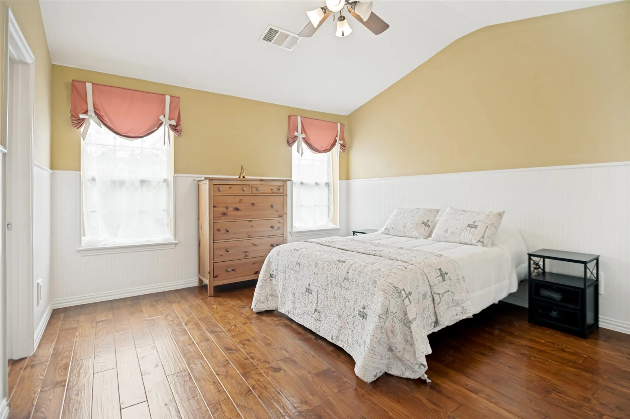 Spacious bedroom featuring wood-finish flooring, white wainscoting, and a vaulted ceiling
