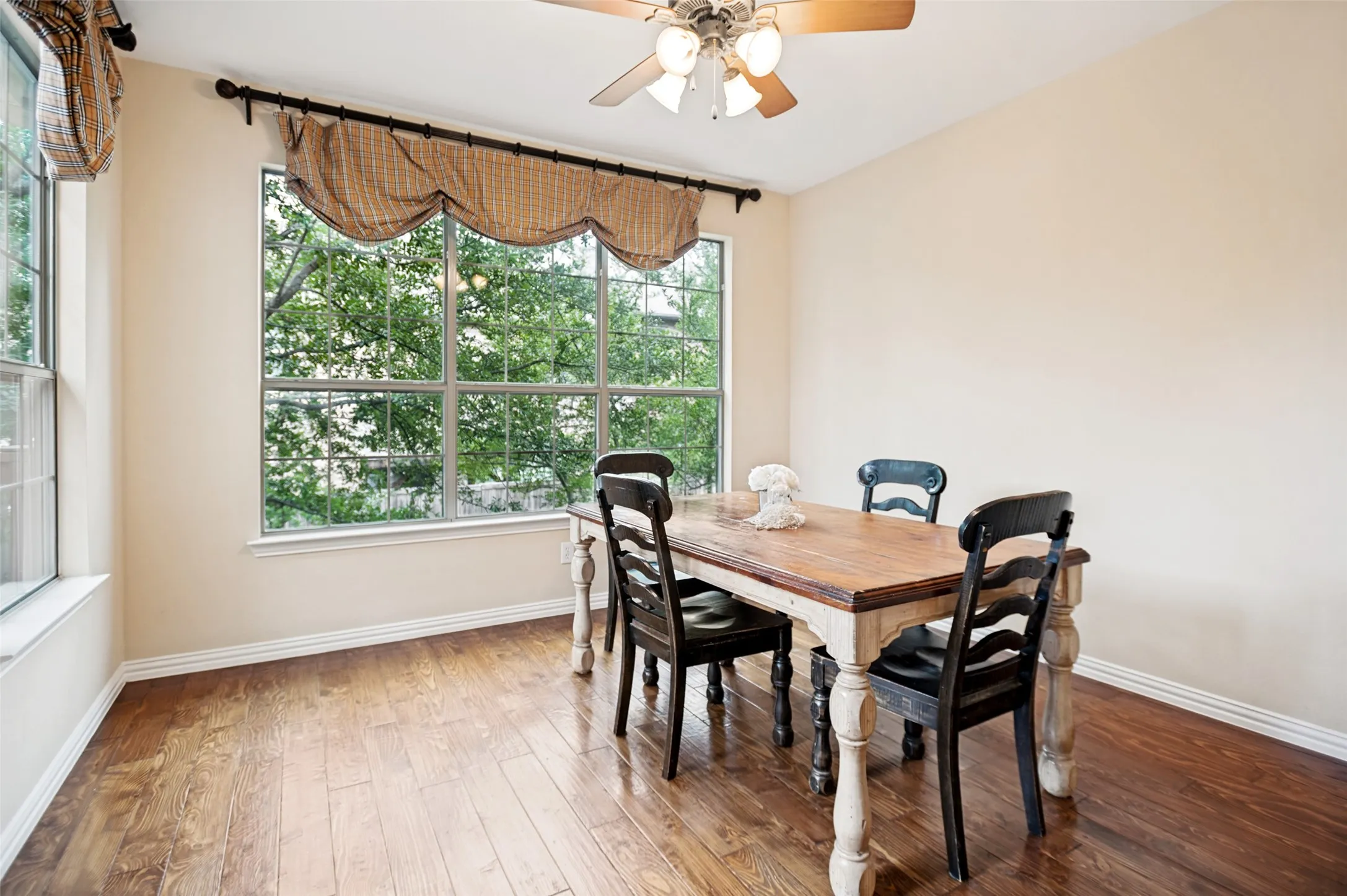 Dining area featuring wood-finish flooring, a multi-pane window with exterior tree views, and a ceiling fan with integrated lighting