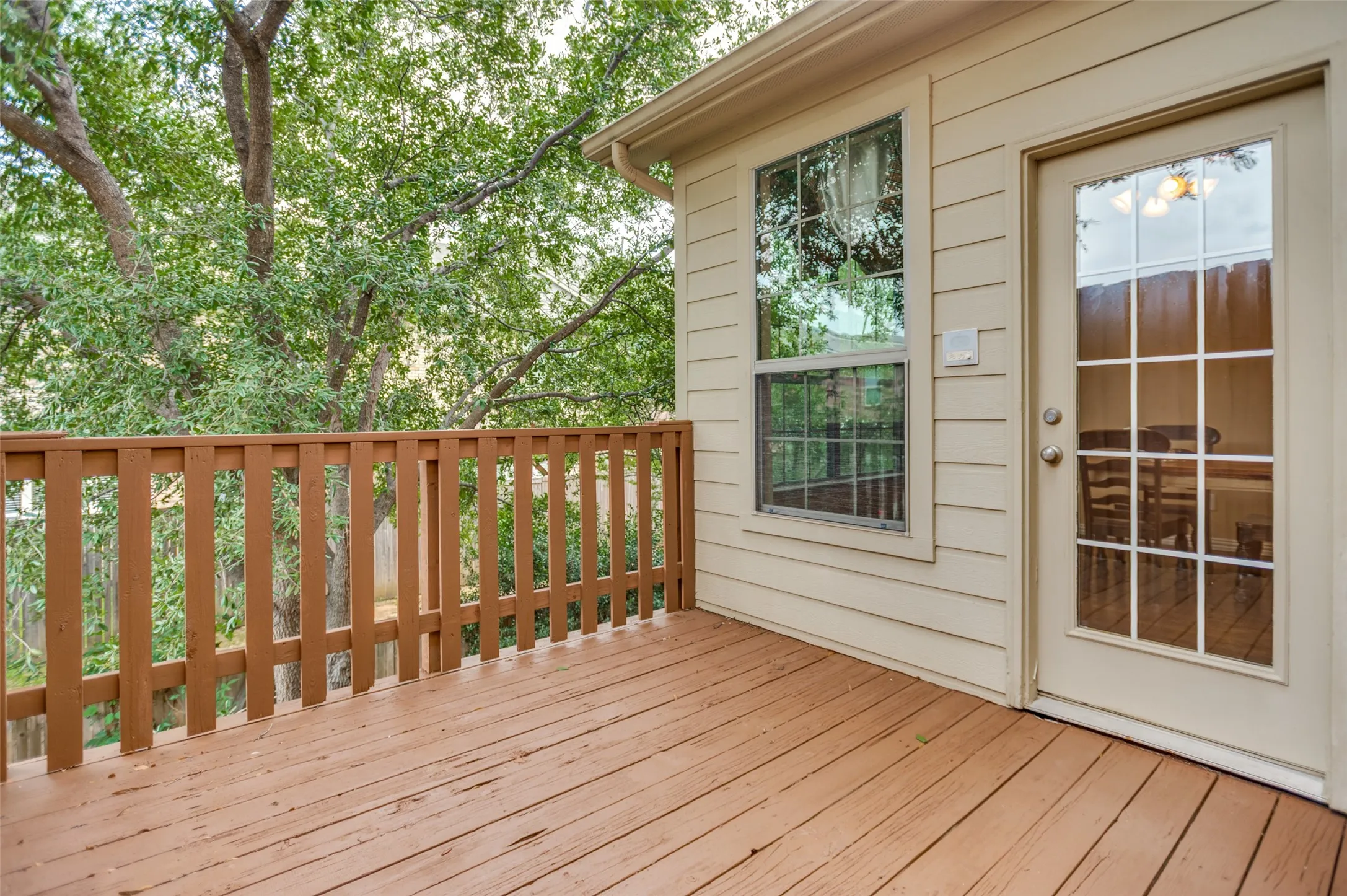 Expansive wooden deck featuring a wooden railing, a large window, a glass-paned door, and siding exterior