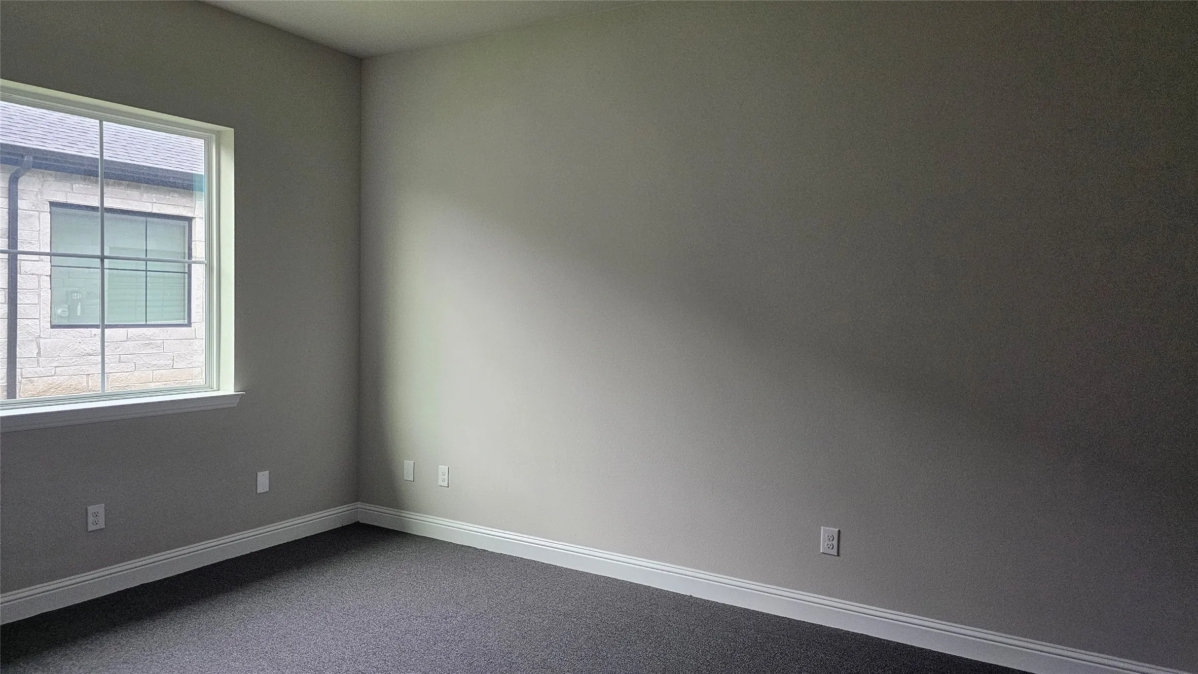 Neutral-toned room with a large window, dark carpet, and white baseboards
