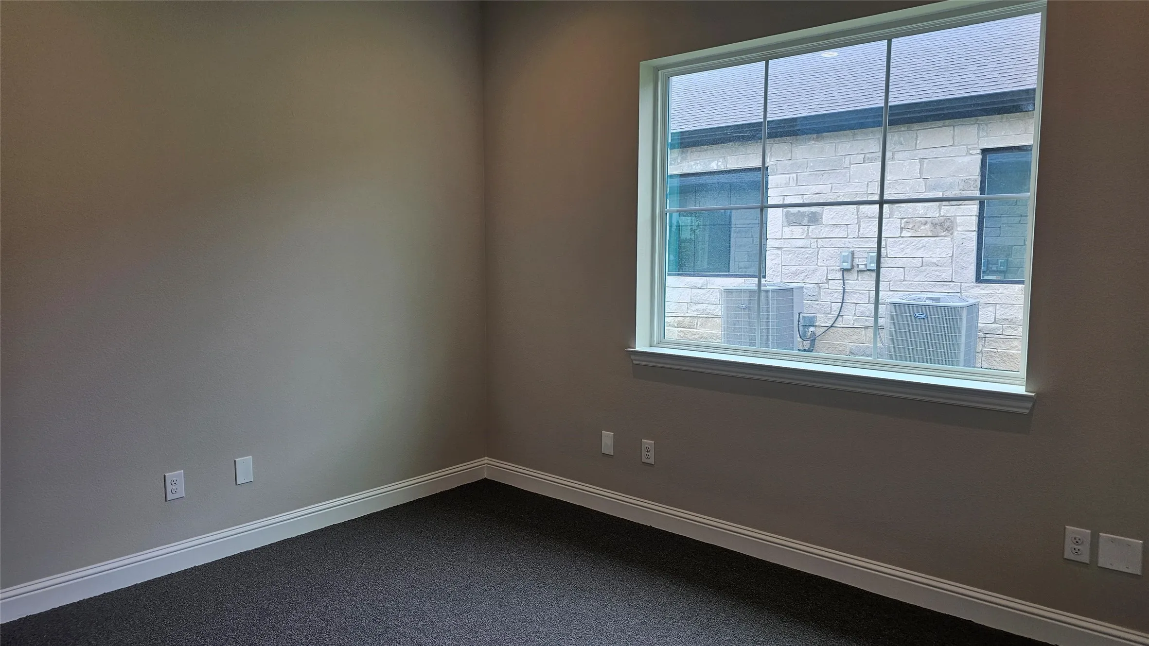Rectangular window with white trim, neutral wall color, dark gray carpet, and white baseboards