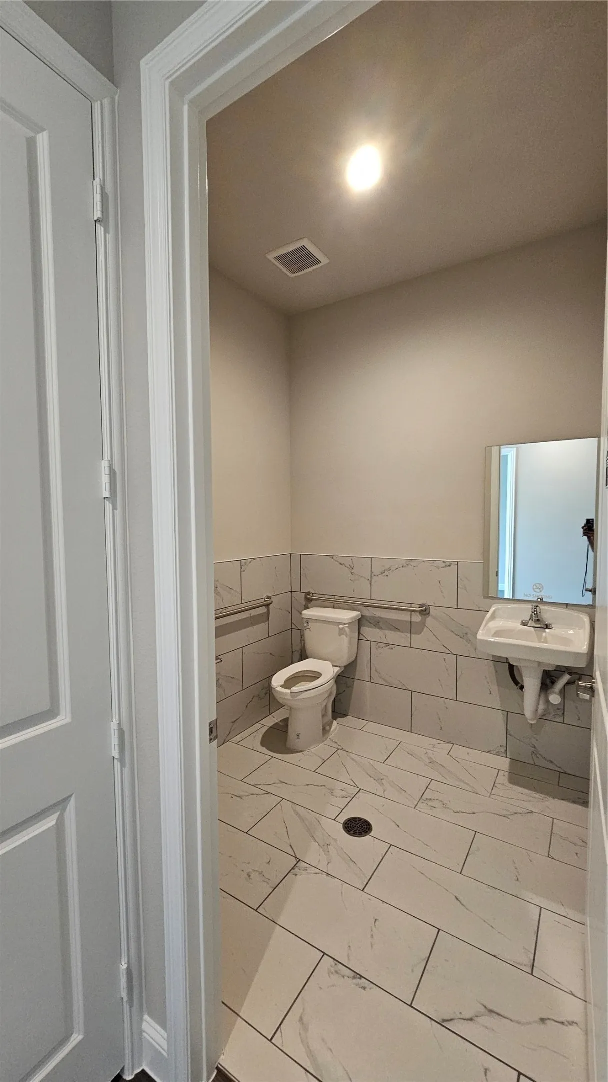 Bathroom featuring white rectangular wall and floor tiles, a pedestal sink, and a commode