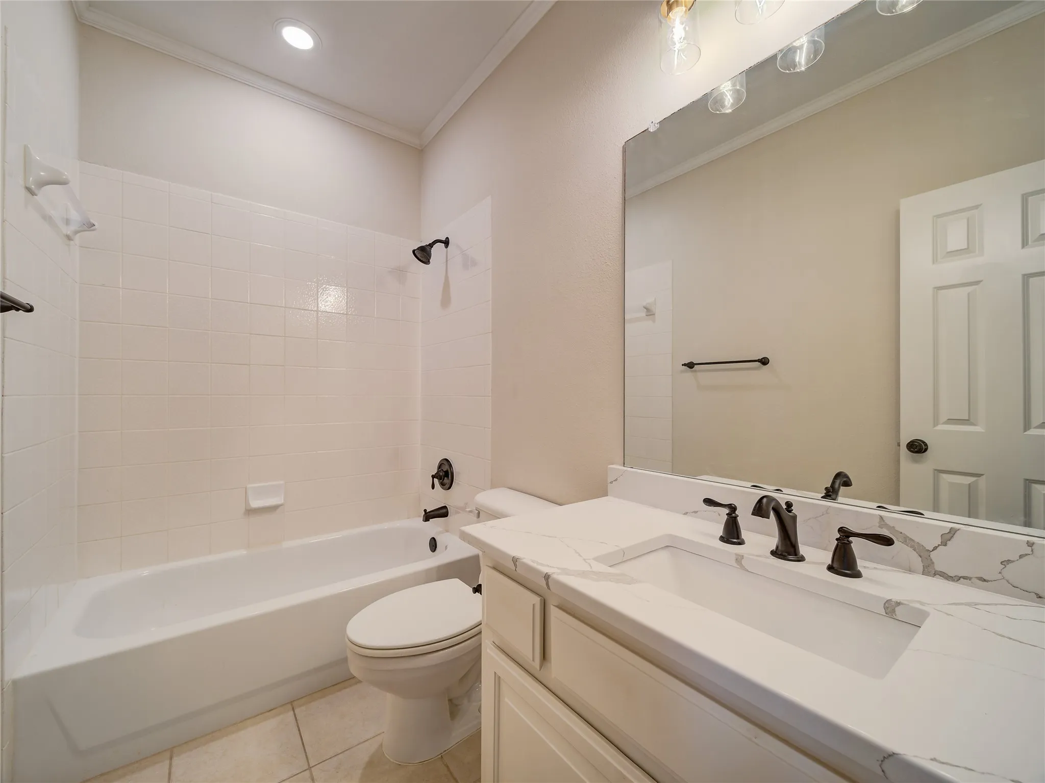 Bathroom featuring a white bathtub with tile surround, a built-in vanity with a white countertop and integrated sink, oil-rubbed bronze fixtures, and a large mirror with overhead lighting