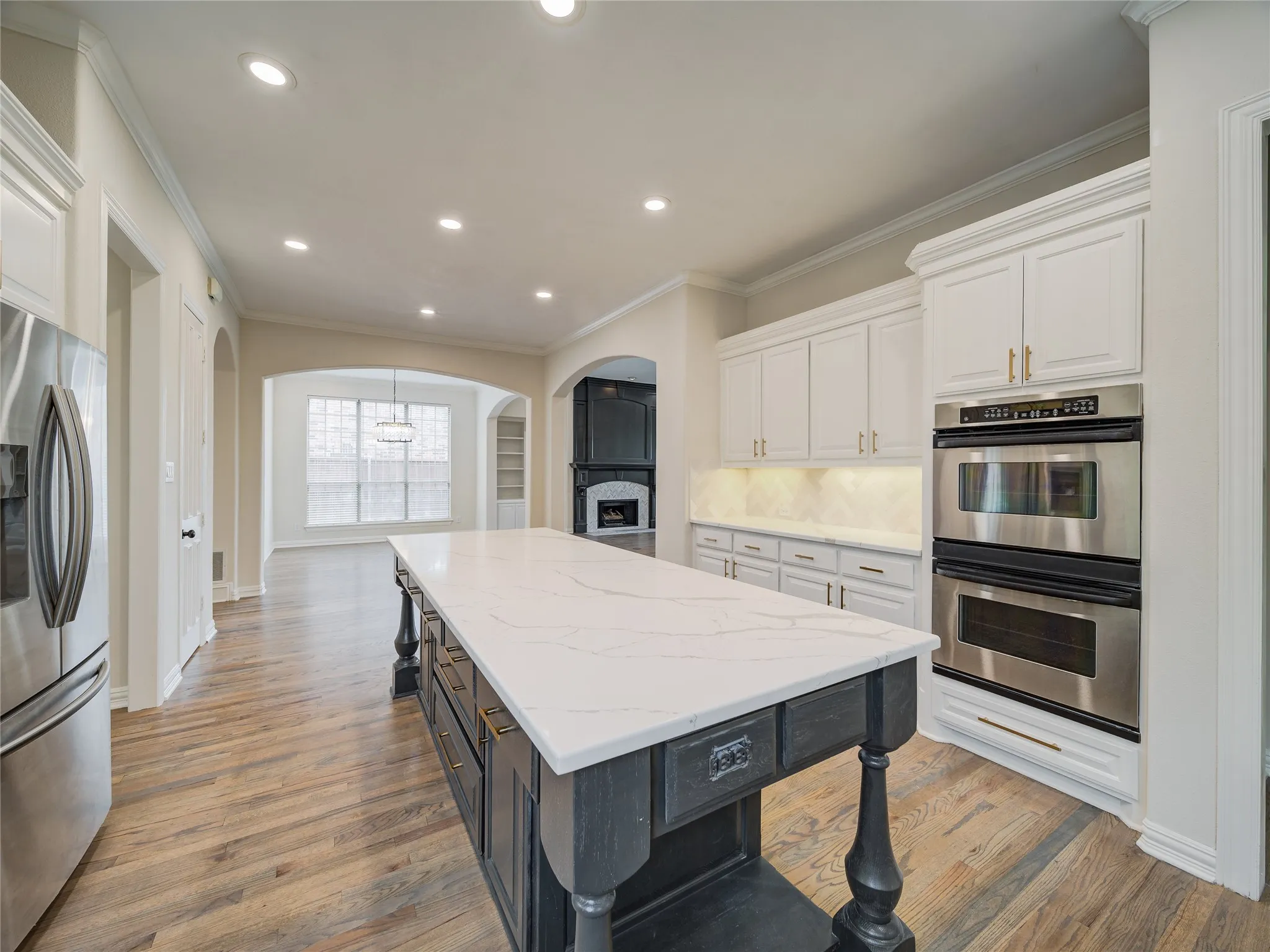 Kitchen featuring an oversized island with a white stone countertop, white cabinetry with gold-tone hardware, stainless steel double wall ovens, and wood-finish flooring