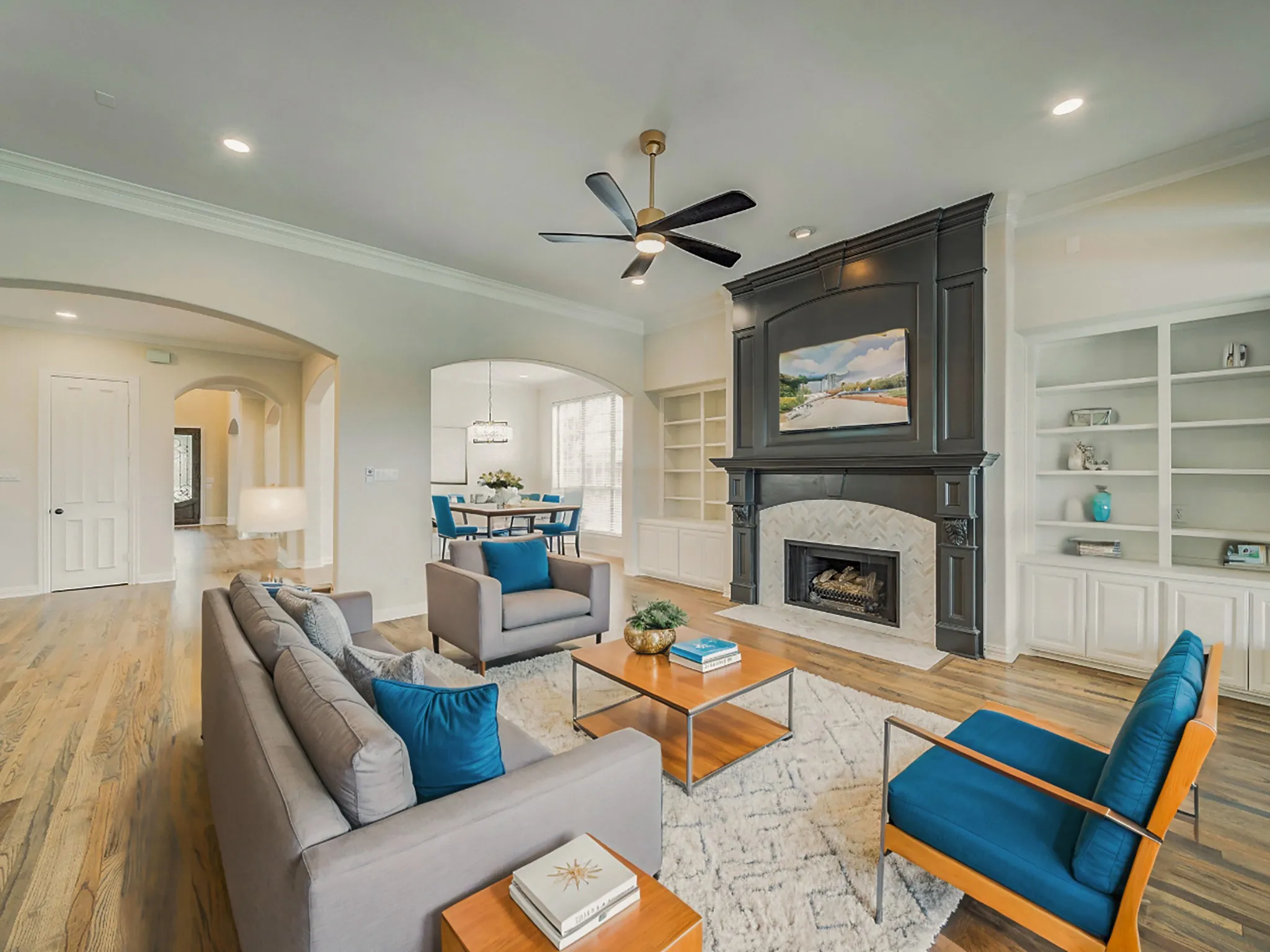 Spacious living area featuring wood-finish flooring, a decorative fireplace with a dark wood mantel and light-toned tile surround, and built-in shelving with cabinetry