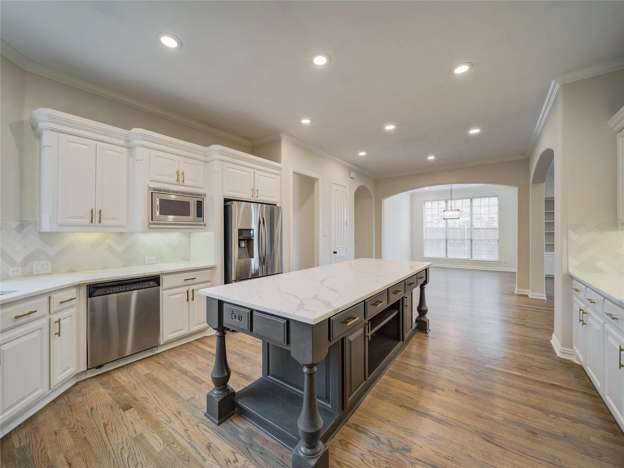 Kitchen featuring a substantial island with a light-toned countertop, wood-finish flooring, recessed lighting, white cabinetry, and stainless steel appliances including a refrigerator, microwave, and dishwasher