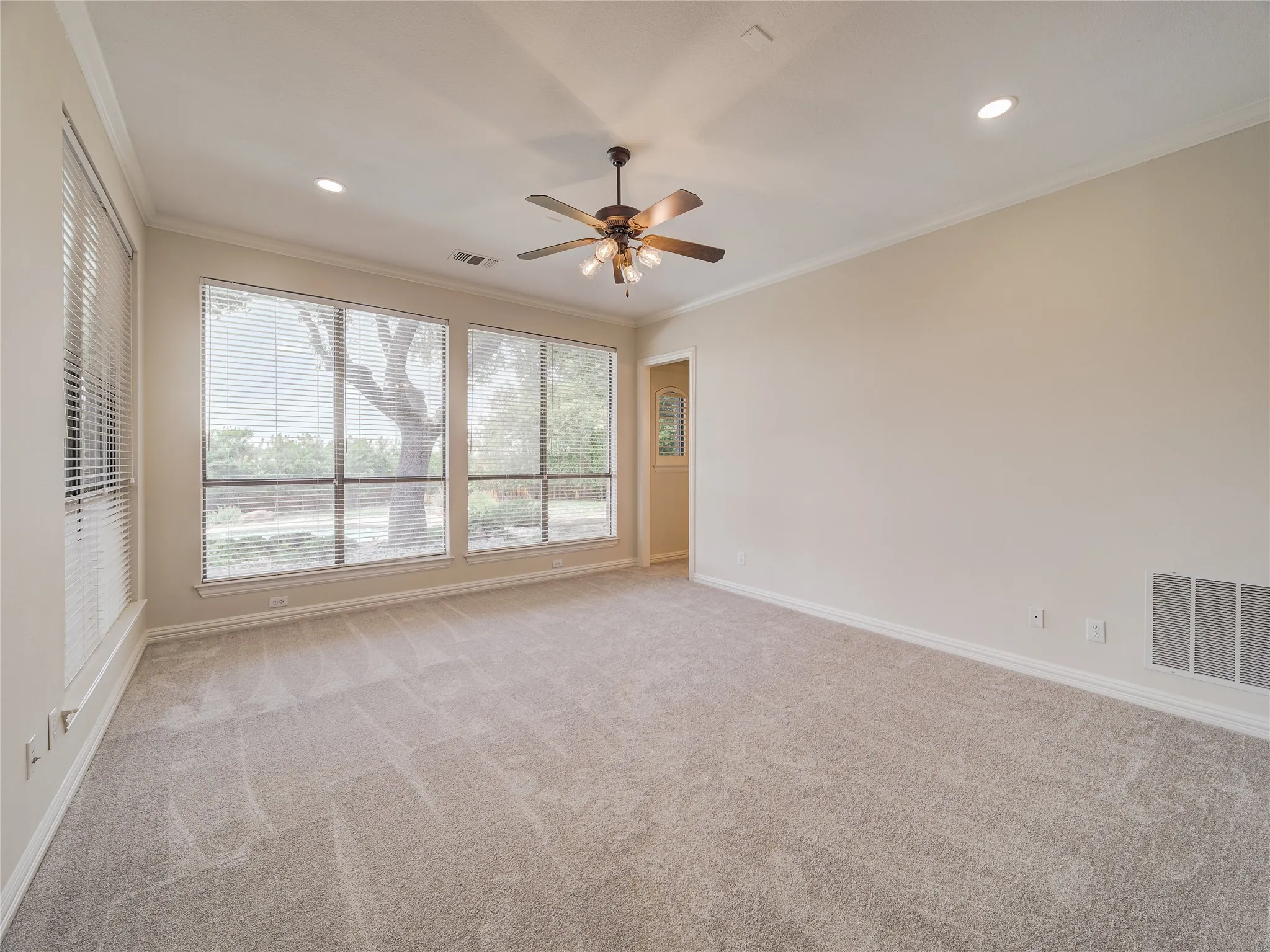 Spacious room featuring broad windows with blinds, recessed lighting, a ceiling fan, crown molding, and neutral-toned carpeting