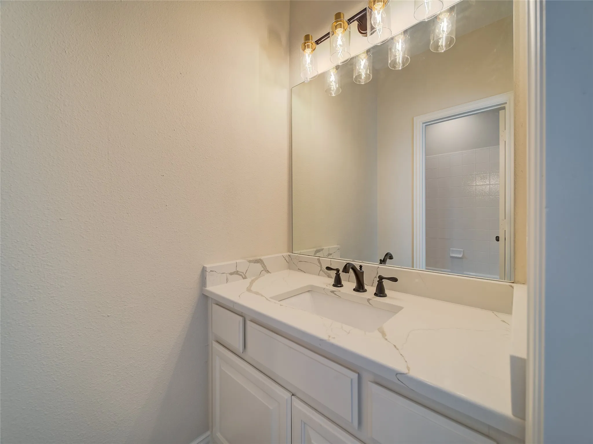 Bathroom vanity featuring a single basin, stone-look countertop, dark bronze-finish faucet, and a wall-mounted mirror