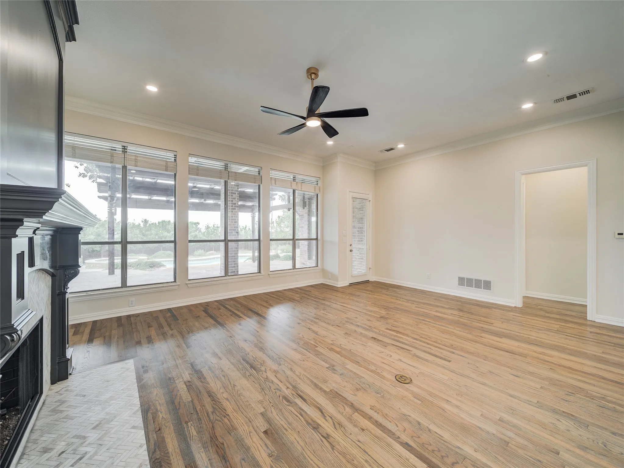 Spacious living area featuring expansive windows, wood-finish flooring, a detailed fireplace with a tile hearth, crown molding, and recessed lighting