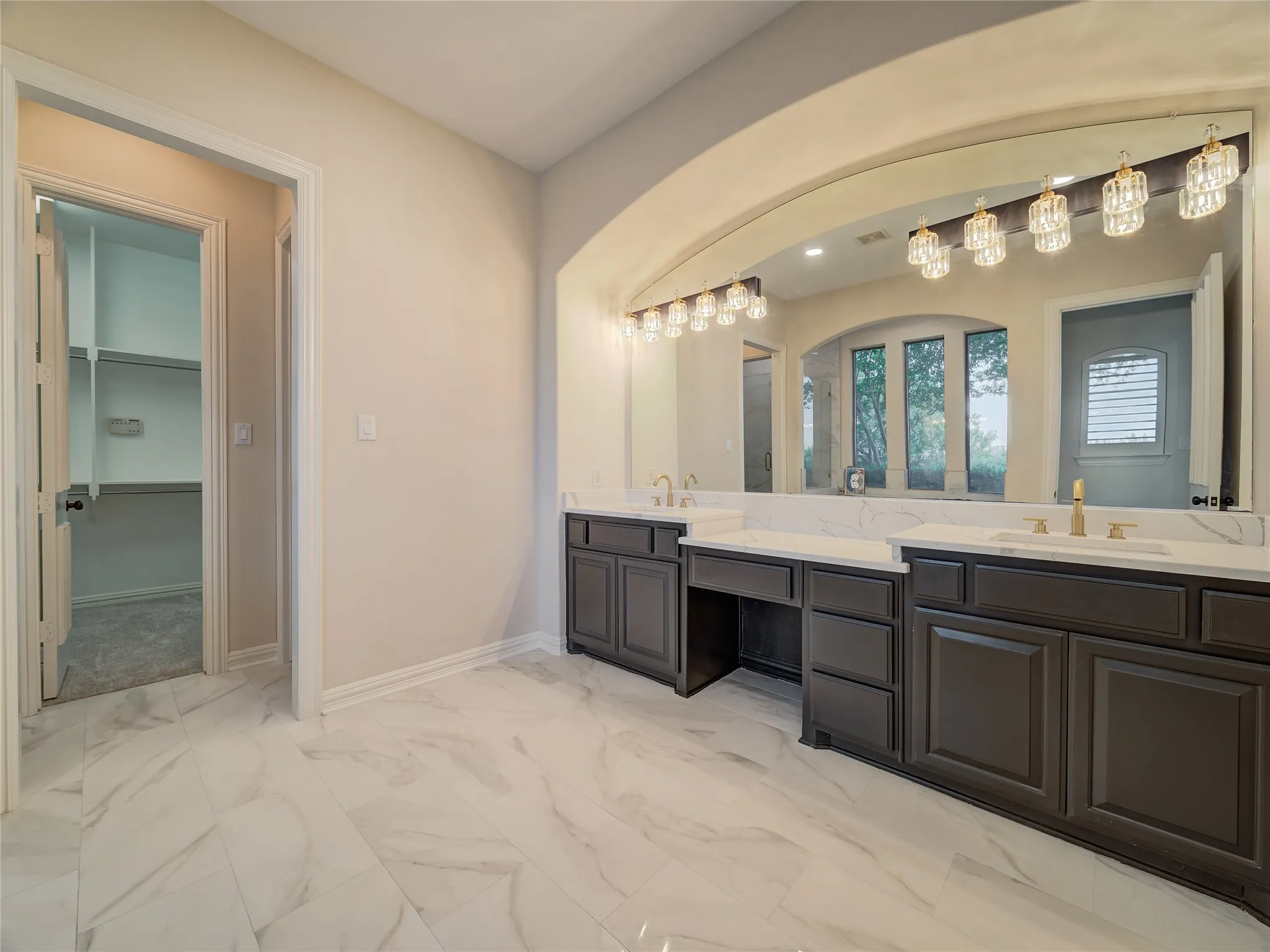 Spacious bathroom featuring dual vanities with dark cabinetry, integrated sinks, white countertops, and gold-finish fixtures